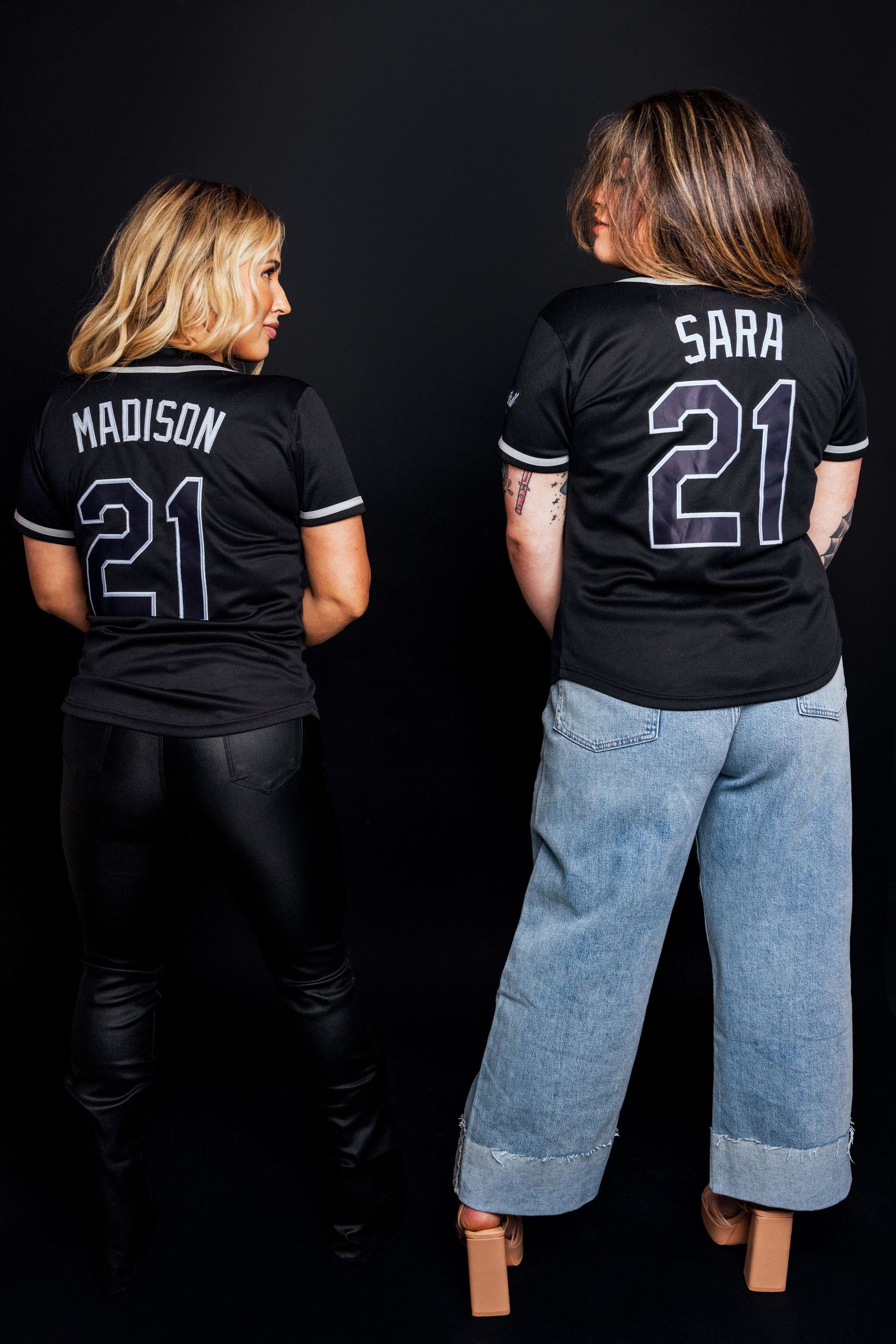 Baseball jersey mockup showing back view of black jerseys with numbers and text against dark background.