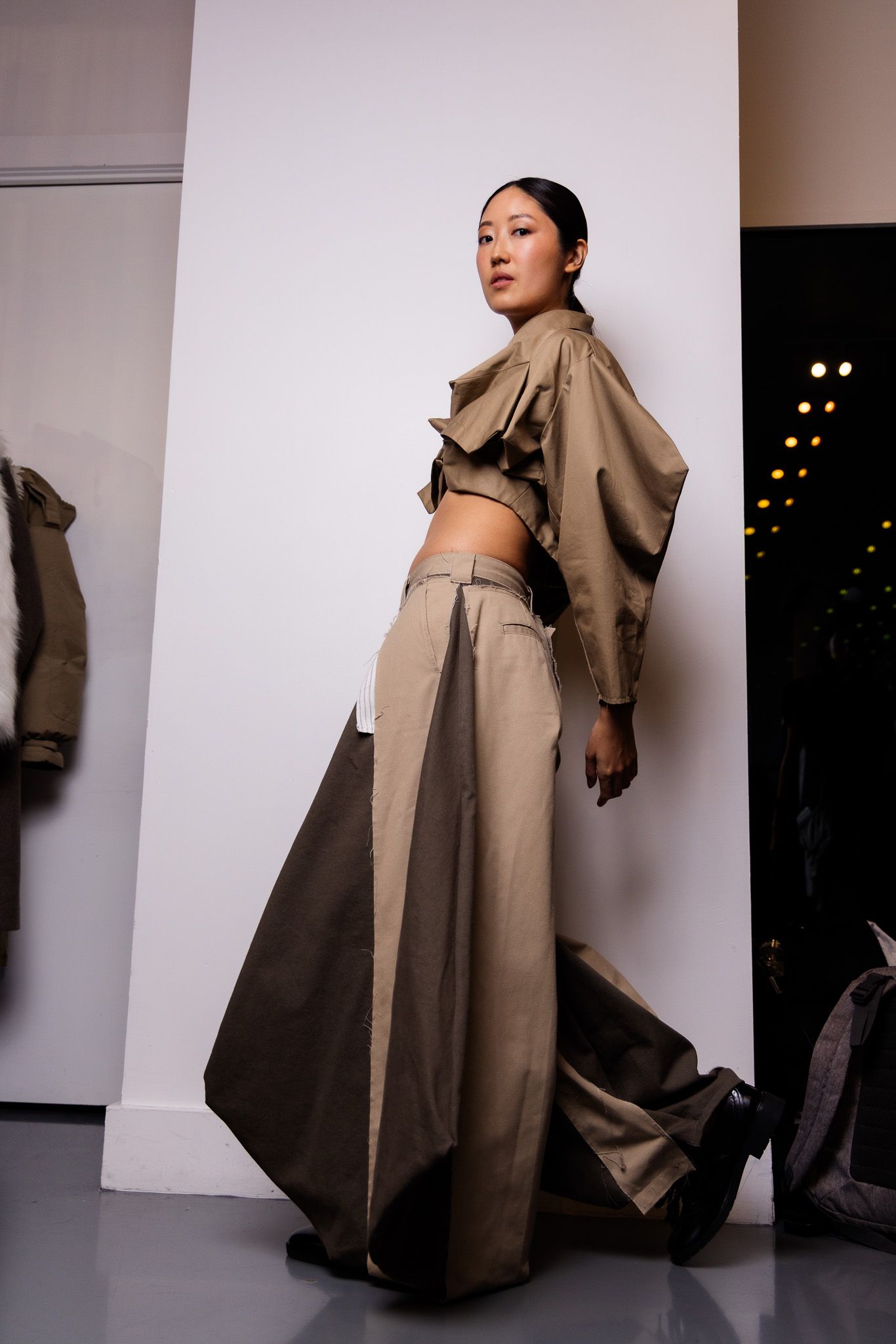 Avant-garde fashion shot featuring oversized beige coat with dramatic draping.