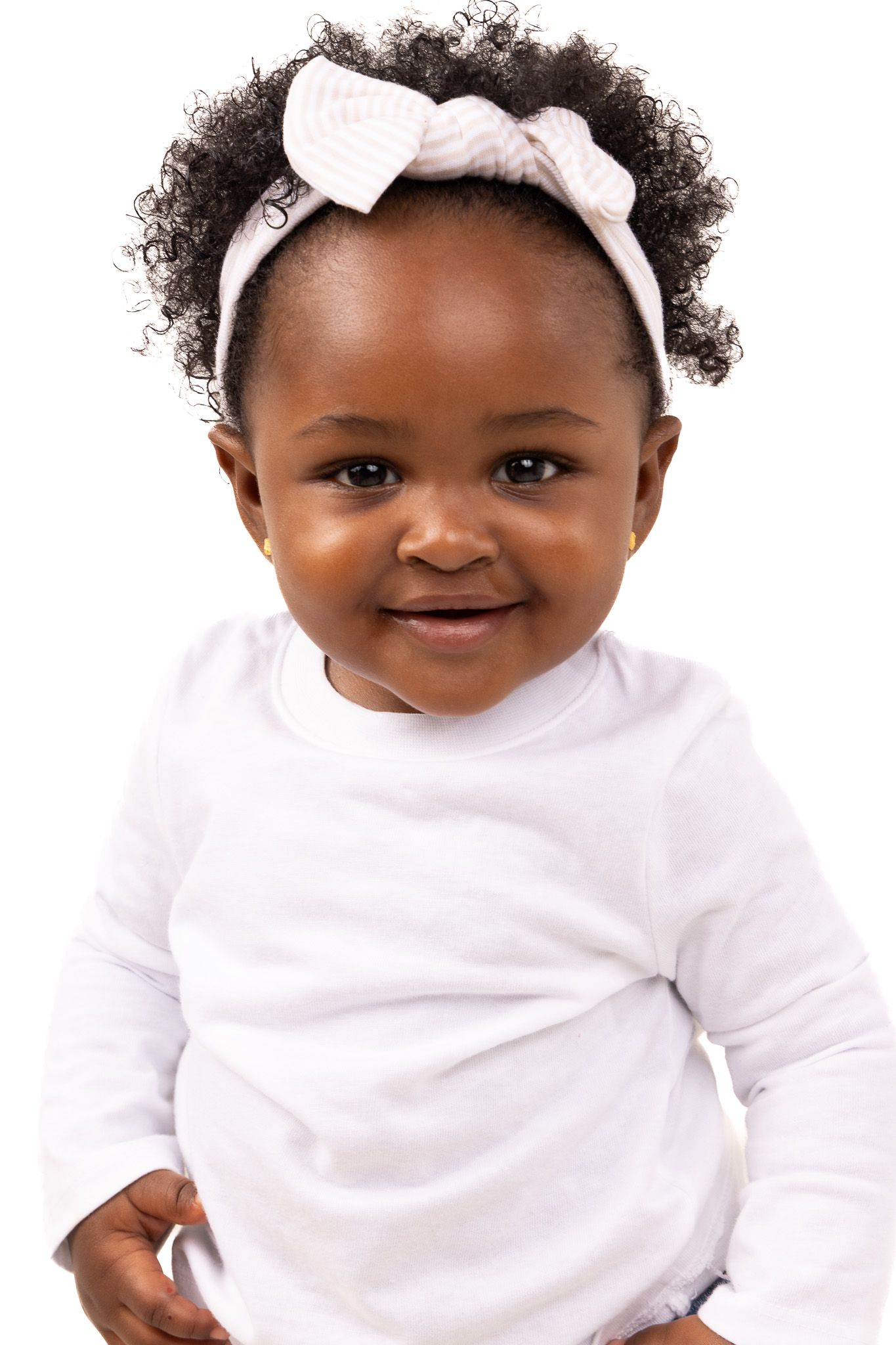Baby in white outfit and bow headband smiling against white background.