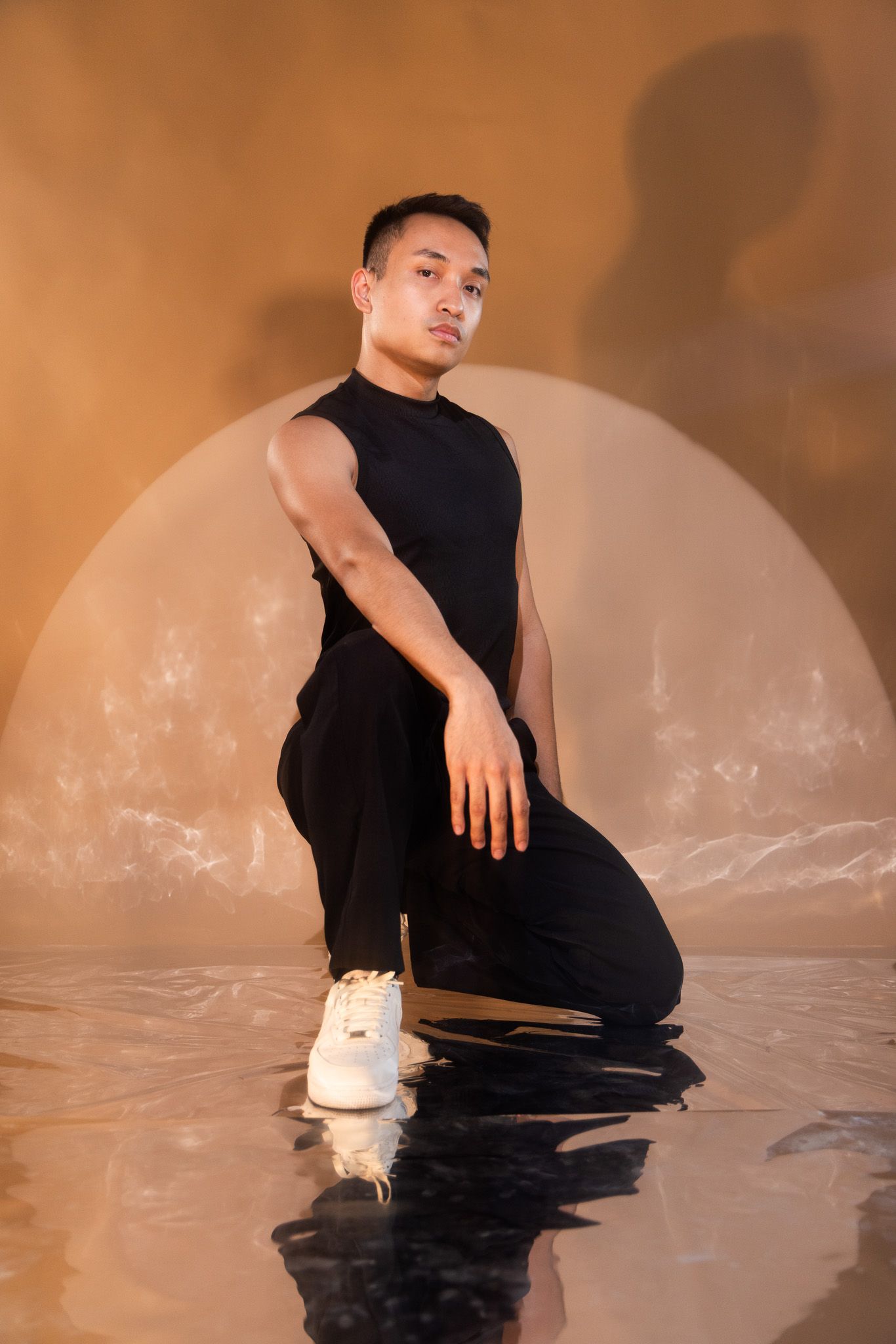 A performer in black clothing poses dramatically in a reflective pool of water with moody lighting.