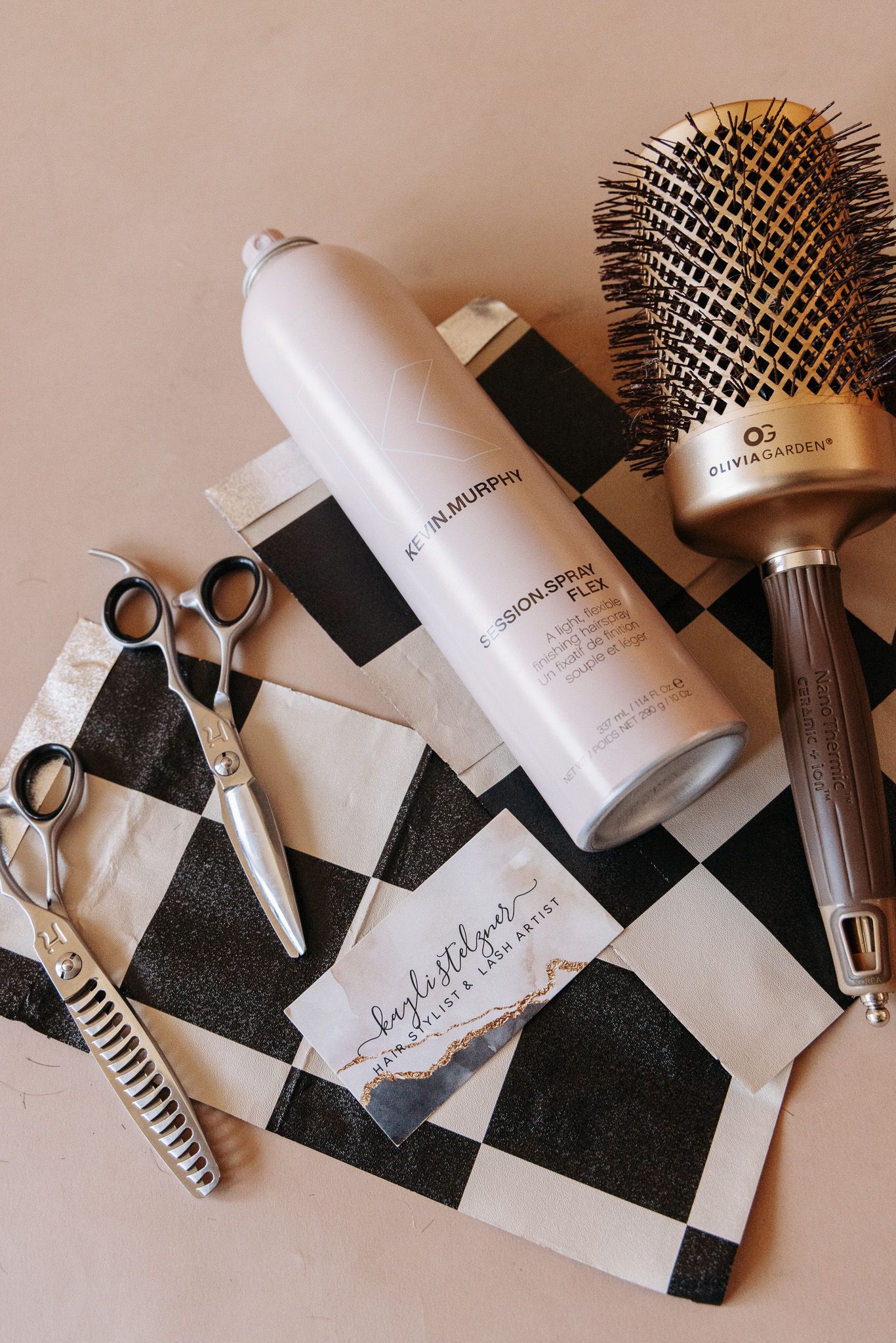 Professional hairstyling tools and products arranged on a black and white checkered surface.