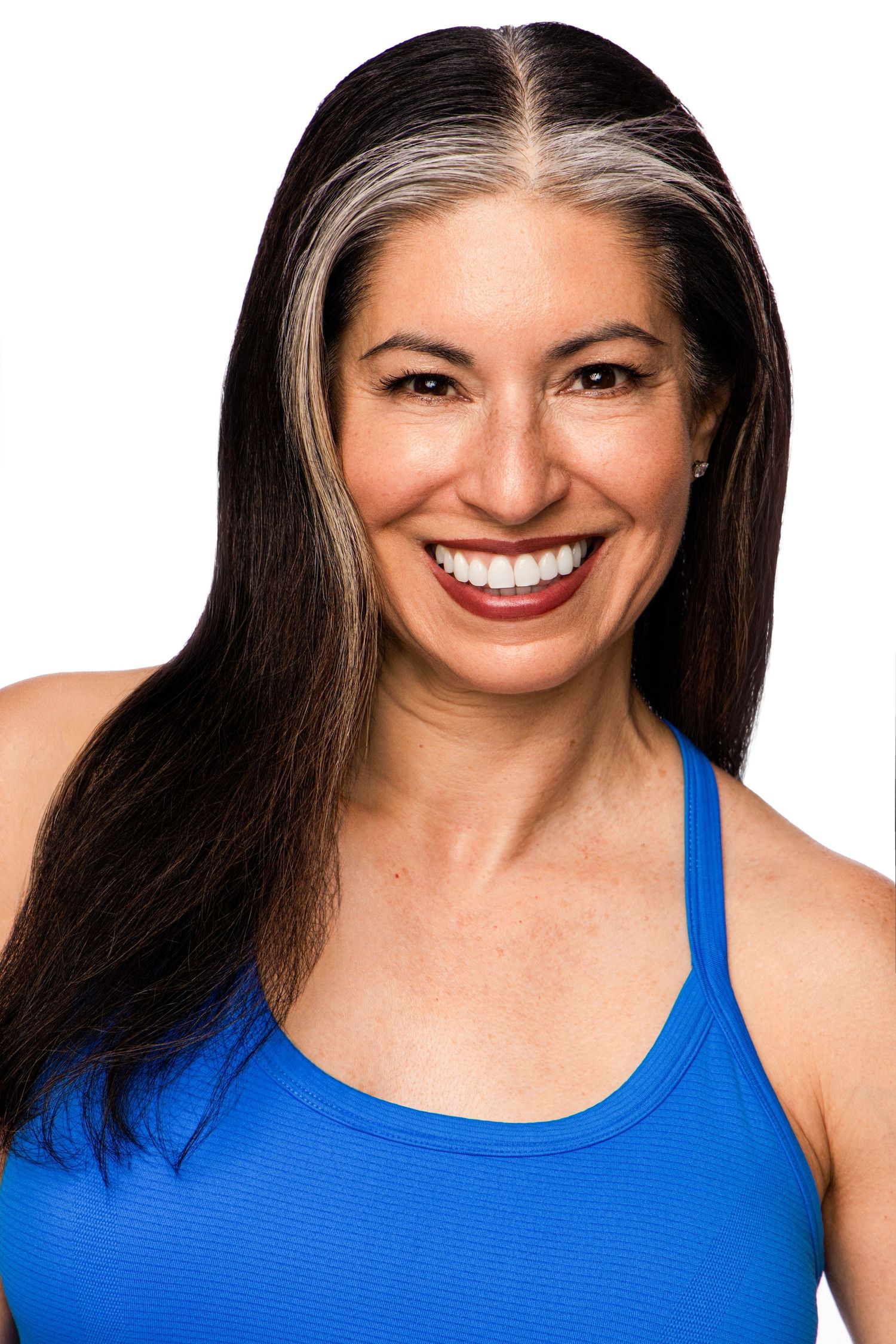 Smiling woman with dark hair and gray highlights wearing a blue tank top on a white background.