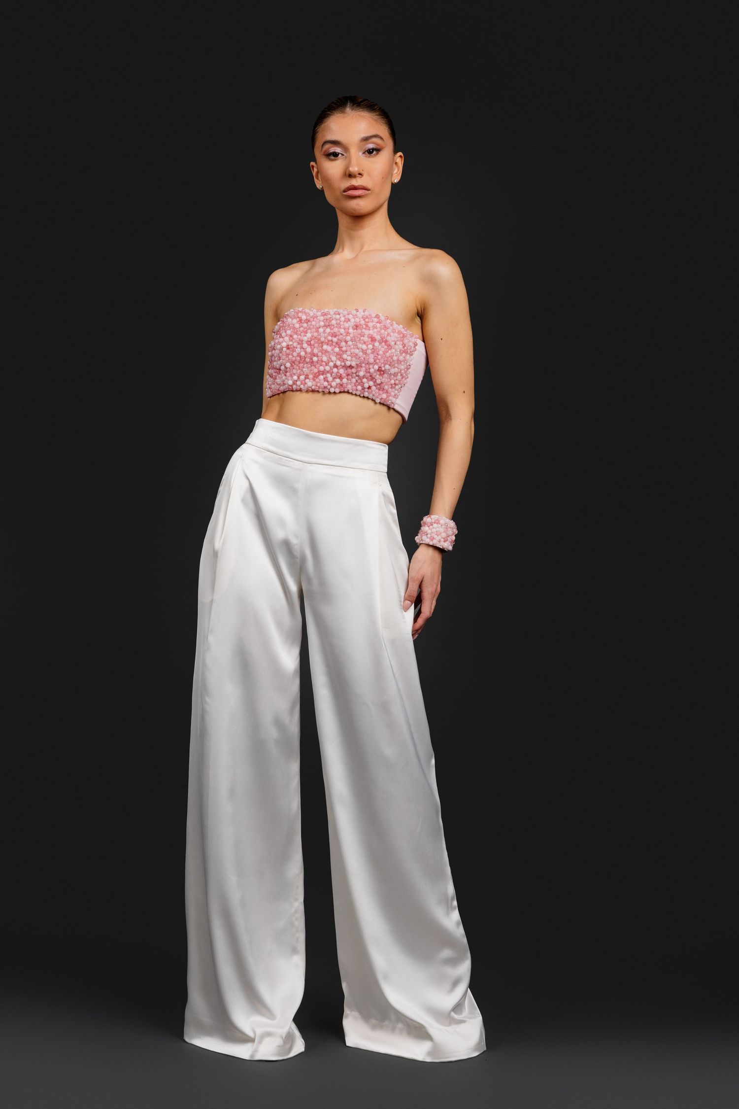 Model wearing pink floral strapless crop top with white wide-leg satin pants and matching bracelet.
