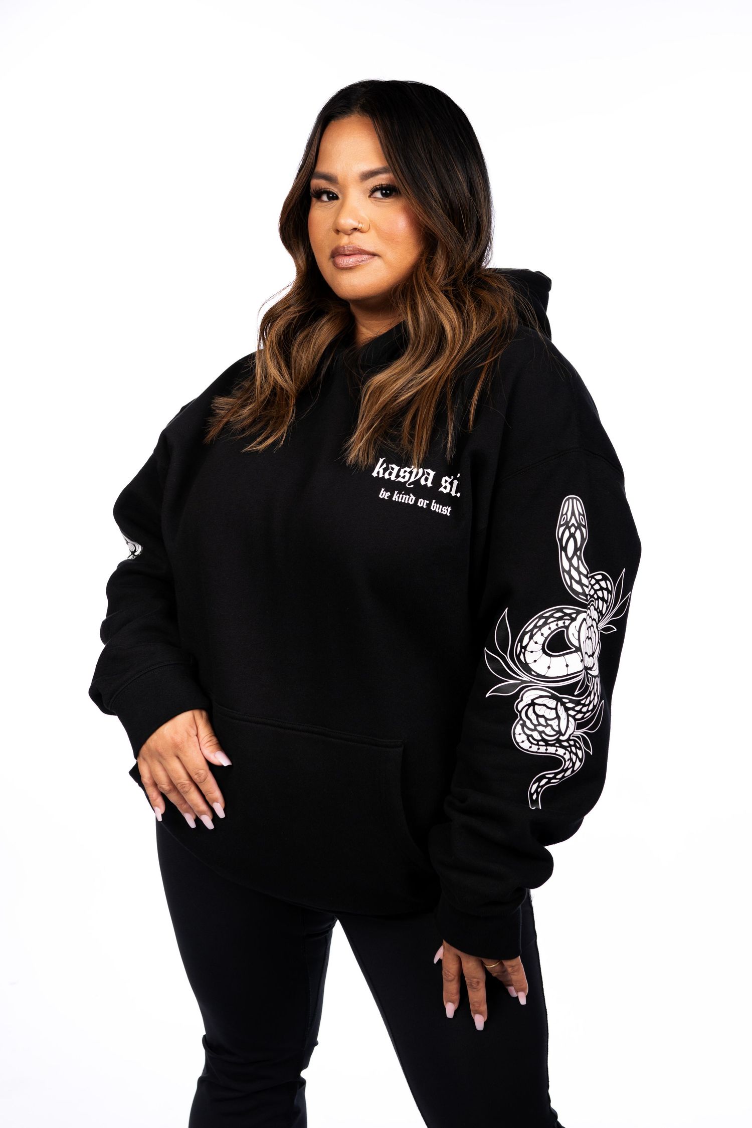 Woman wearing black hoodie with snake graphic on sleeve and text graphic on chest, paired with black leggings.