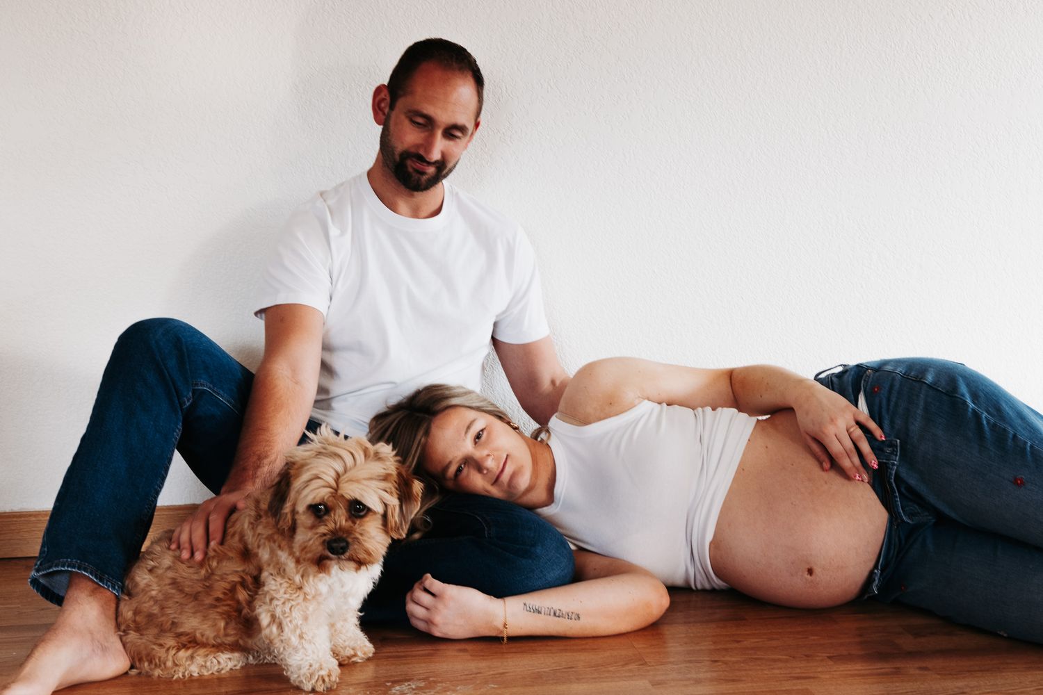 A series of maternity photos showing a couple relaxing on a wooden floor with their small brown dog.