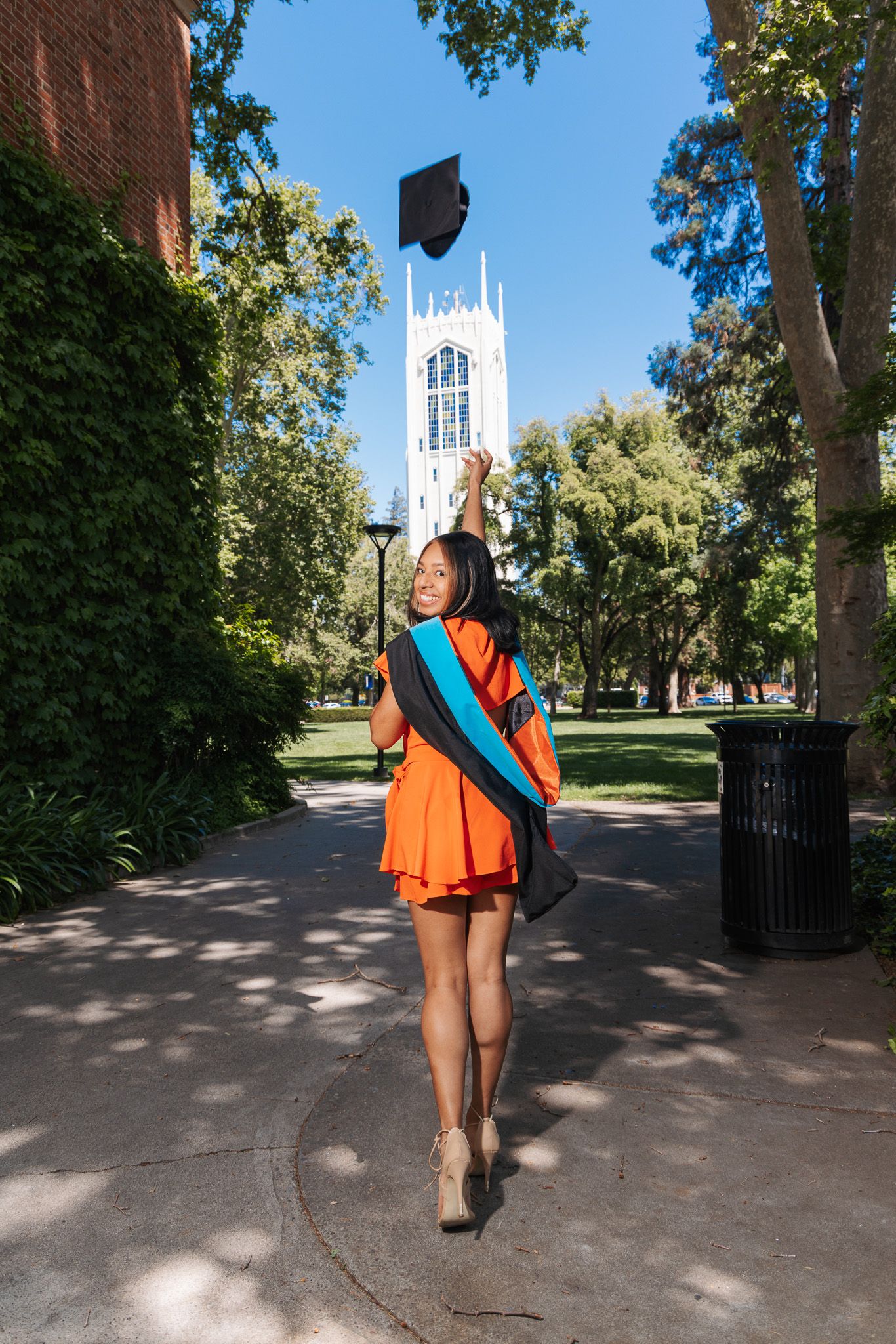 Person in orange and blue outfit walking along tree-lined campus path with white church steeple visible in background.