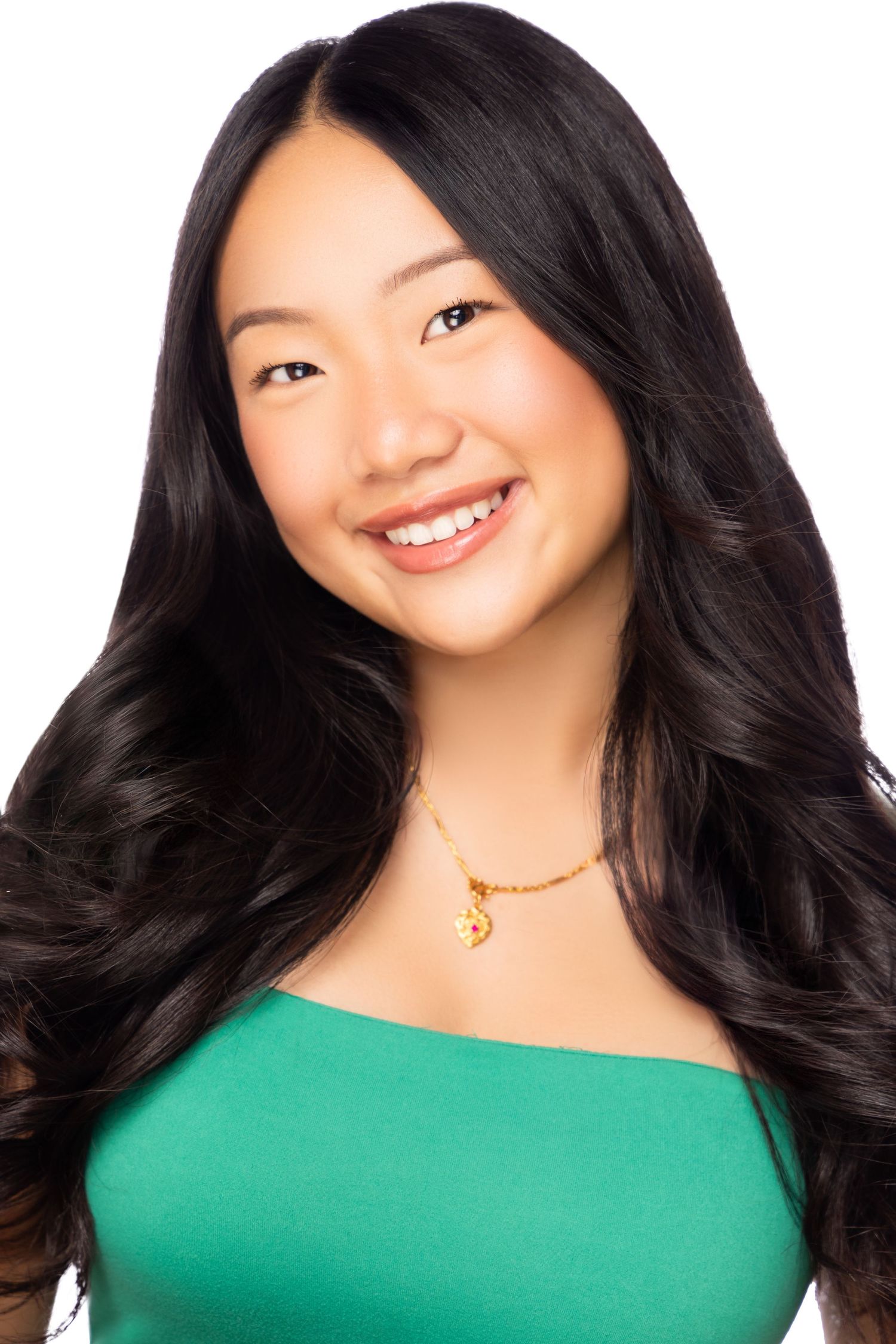 Portrait against white background in green off-shoulder top with flowing black hair and gold necklace.