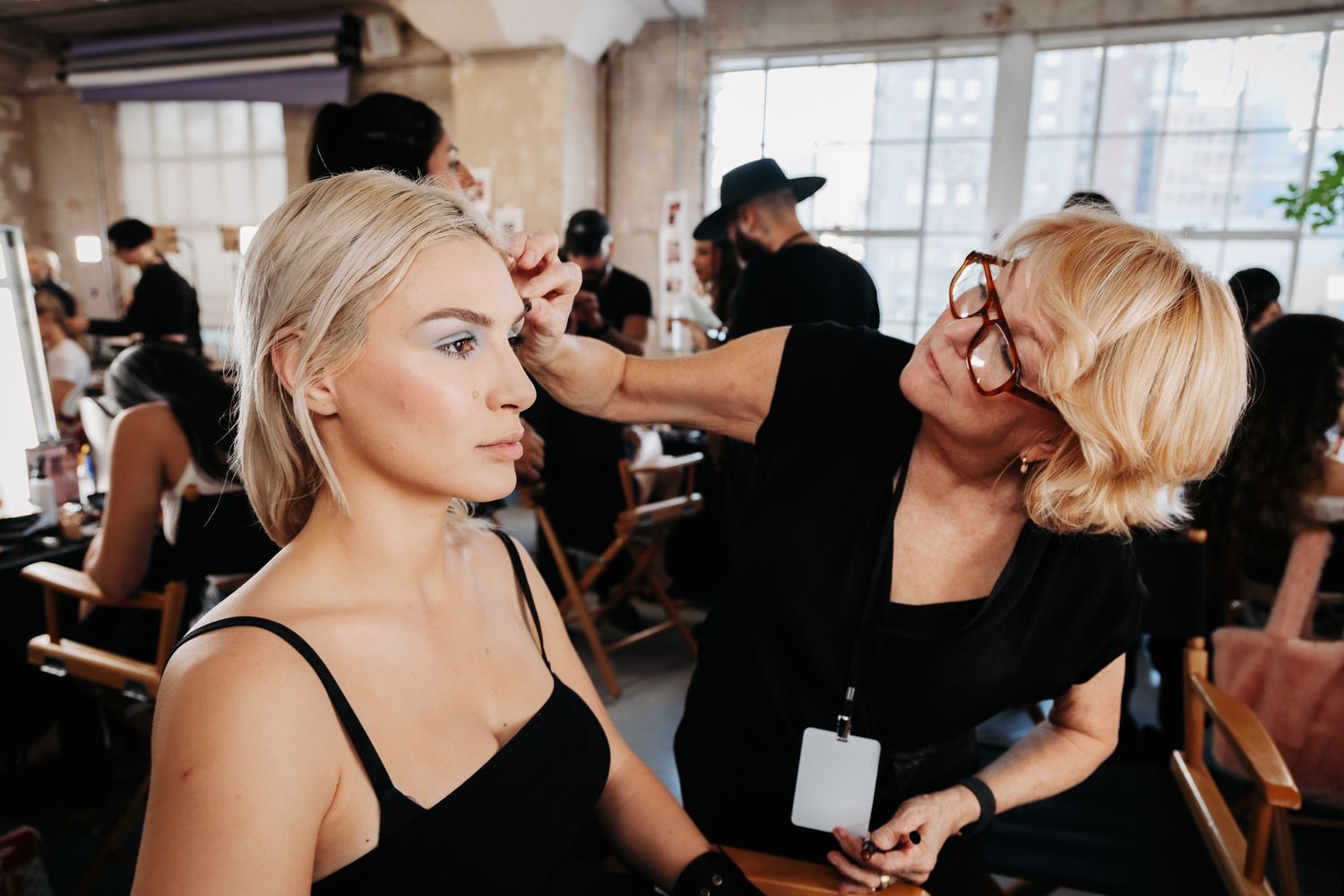 Wedding hair and makeup artists work on several brides and bridesmaids getting ready in elegant dressing room space.