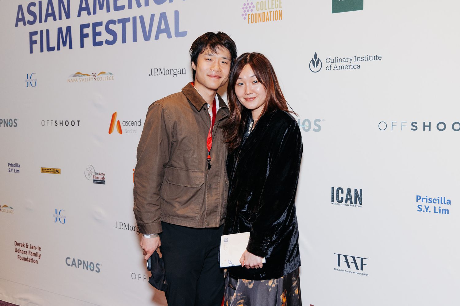 People standing in front of a branded backdrop wall at an Asian American film festival event.