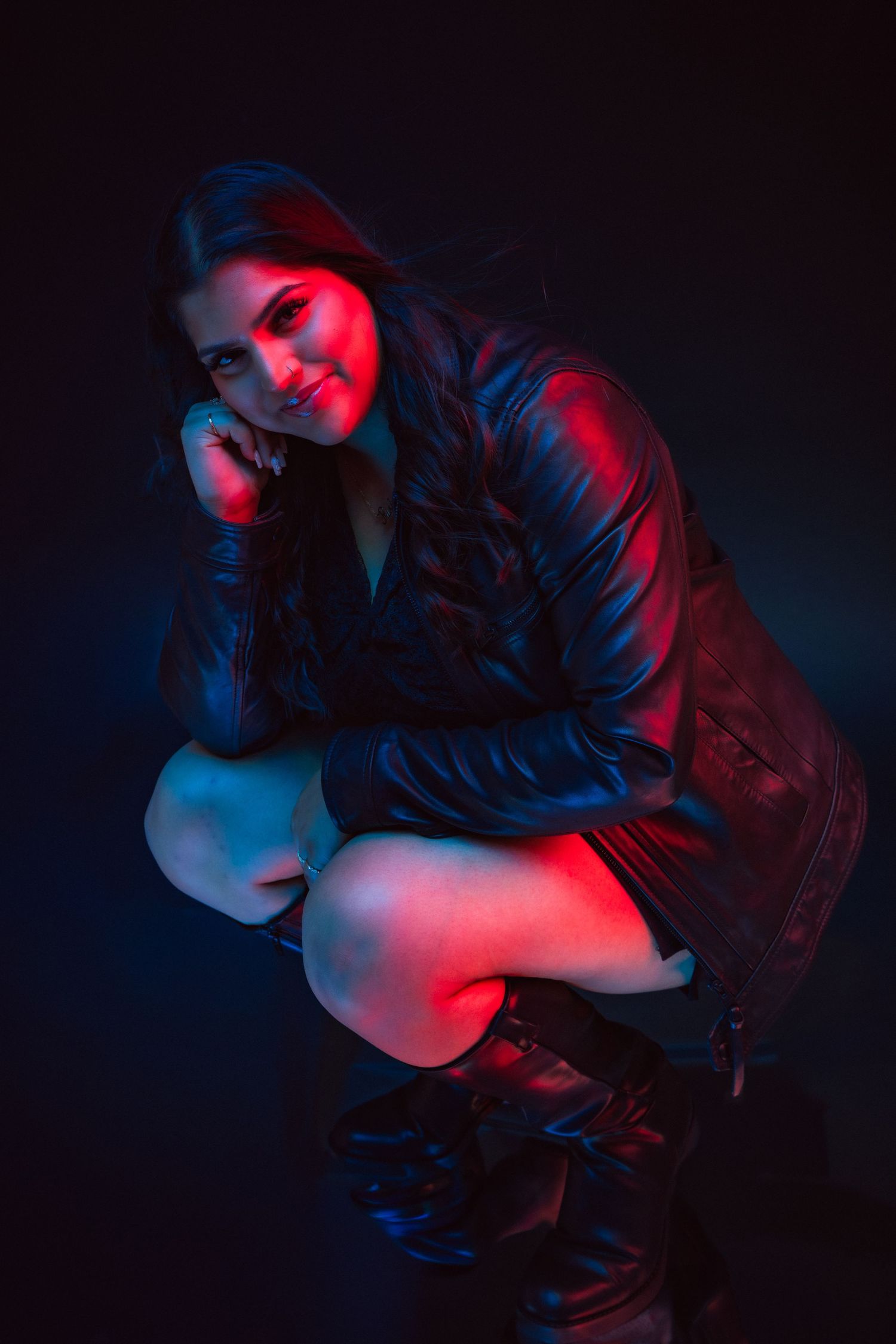 Artistic portrait in dark setting with dramatic red and blue lighting creating moody atmosphere with leather jacket styling.