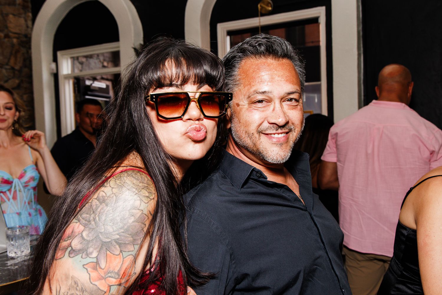 A tattooed woman and a man smiling together at an indoor social gathering or party.
