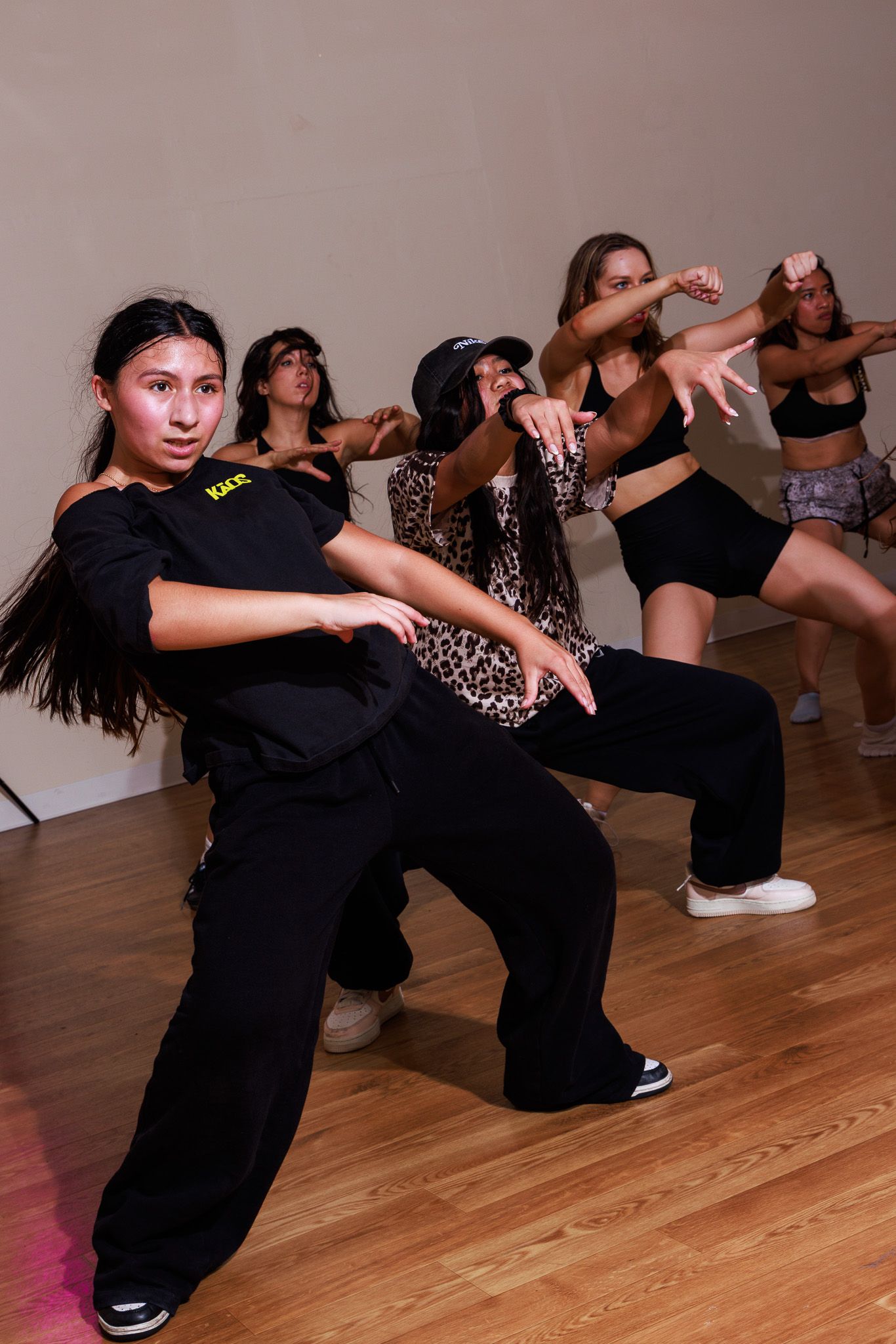 Group of young women performing hip-hop dance moves in a studio with hardwood floors.