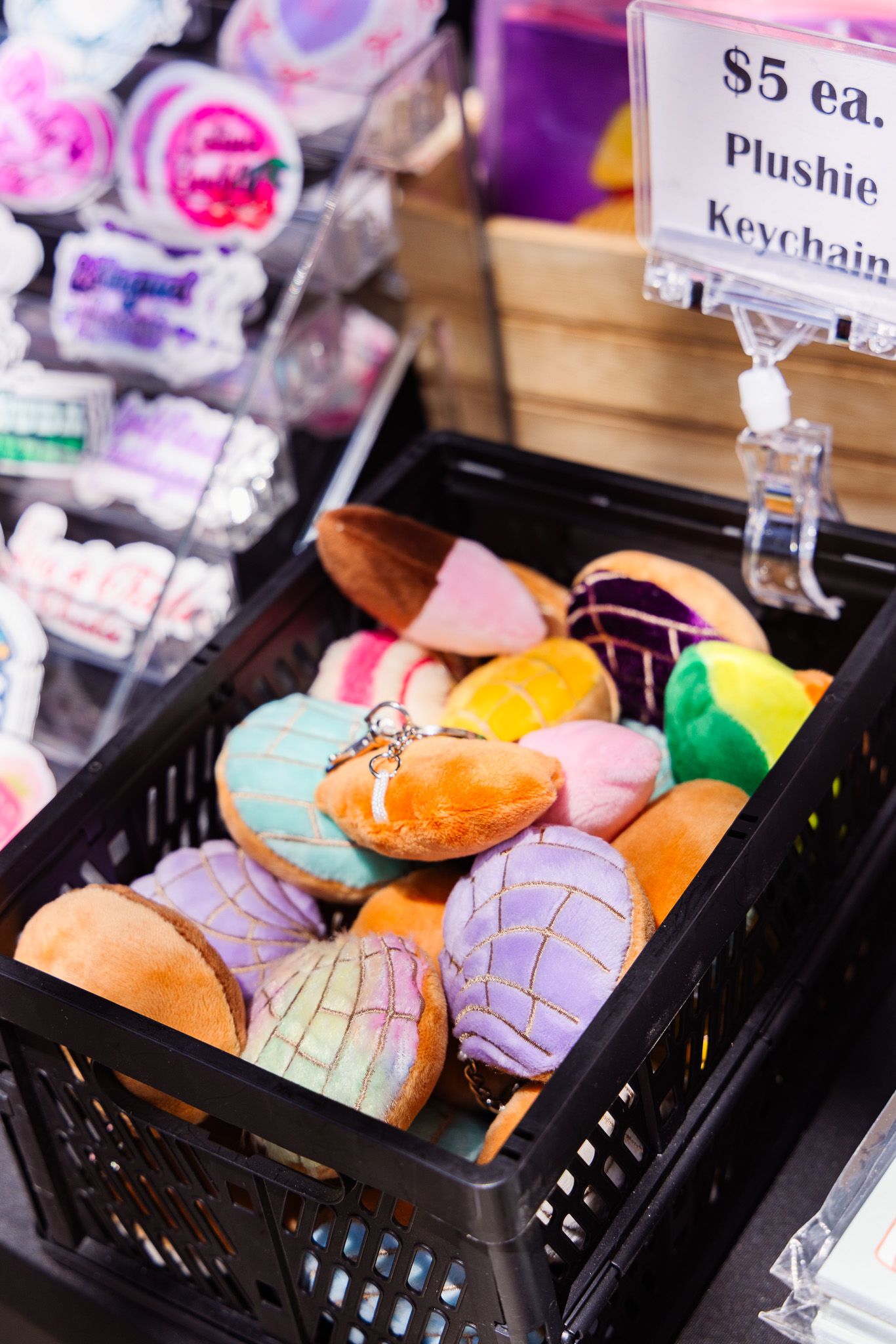 Colorful plushie keychains shaped like seashells displayed in a black basket with a $5 each price sign.