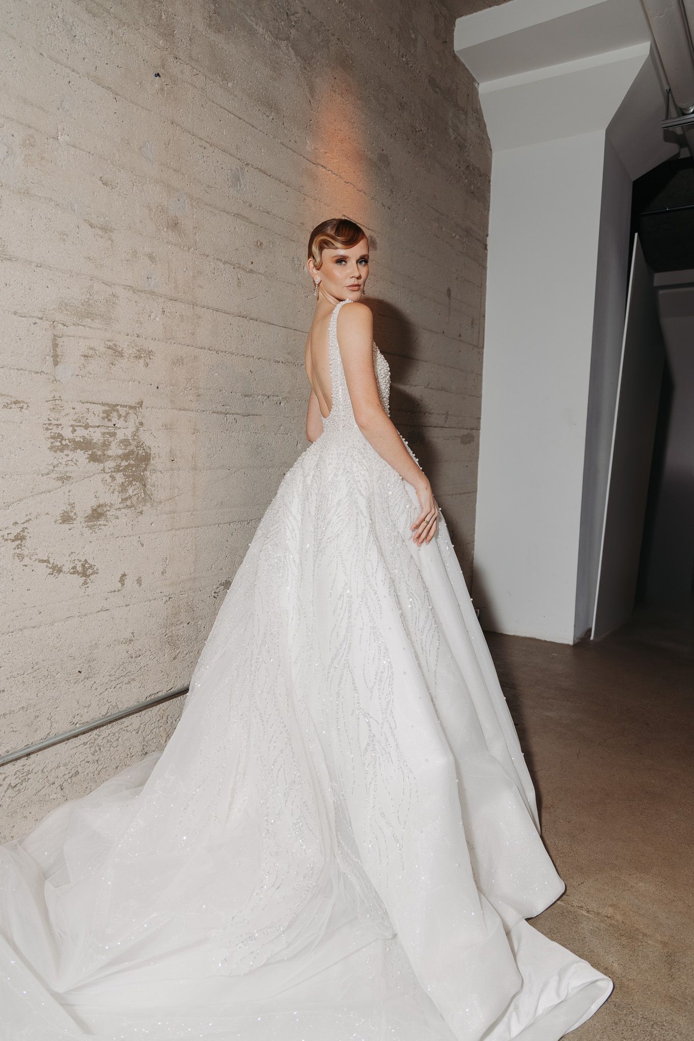 A flowing white wedding gown with a dramatic train photographed against an industrial concrete backdrop.