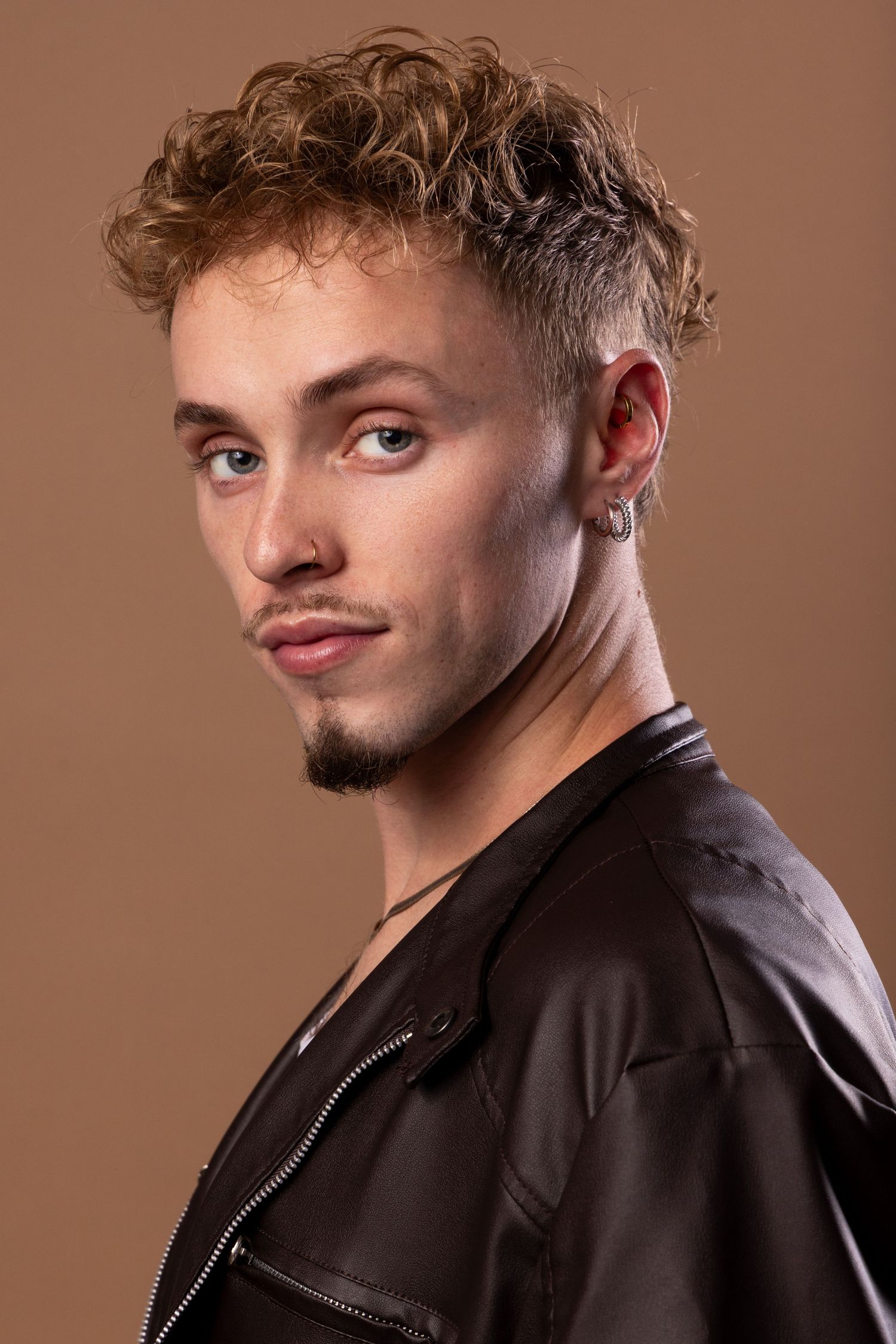 A person in a black leather jacket poses against a brown backdrop in a series of studio portraits.