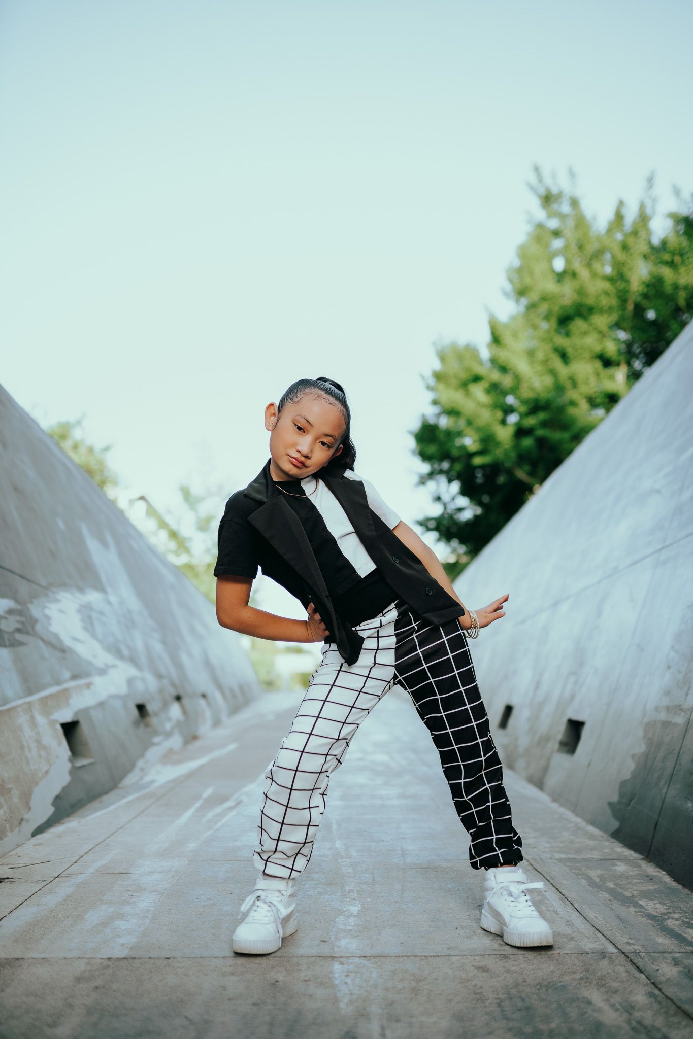 A dynamic dance pose against geometric concrete architecture in black and white street style outfit.