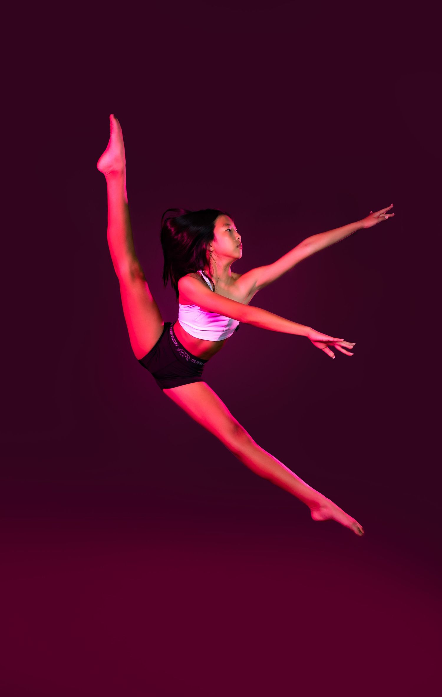 Modern dancer leaps through space illuminated by dramatic red lighting.