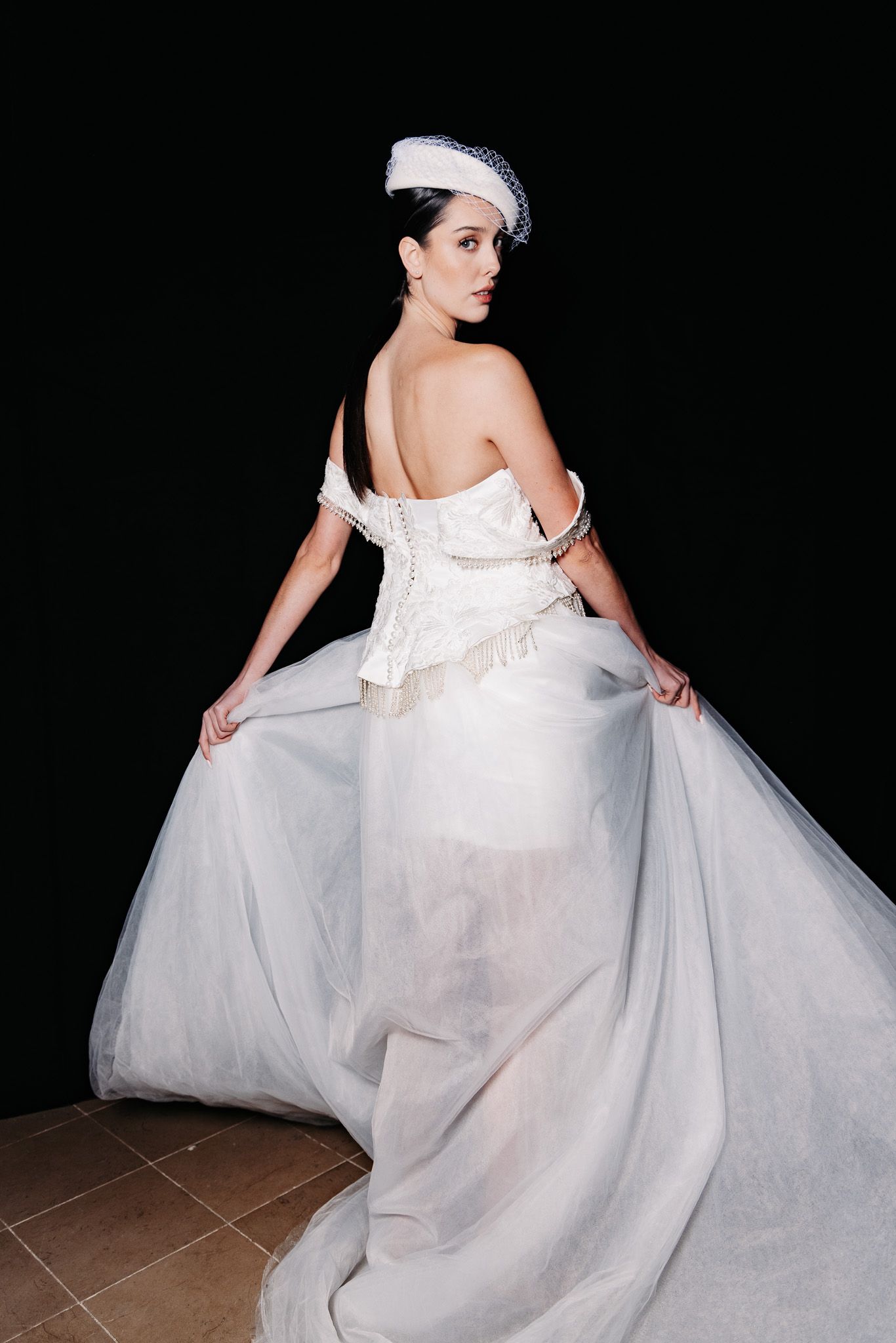 Fashion model wearing a dramatic white tulle ballgown poses against black background in editorial photoshoot.