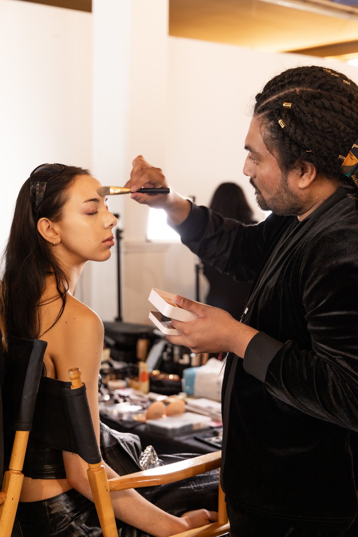 Makeup artist applies cosmetics on model backstage during fashion event preparation.