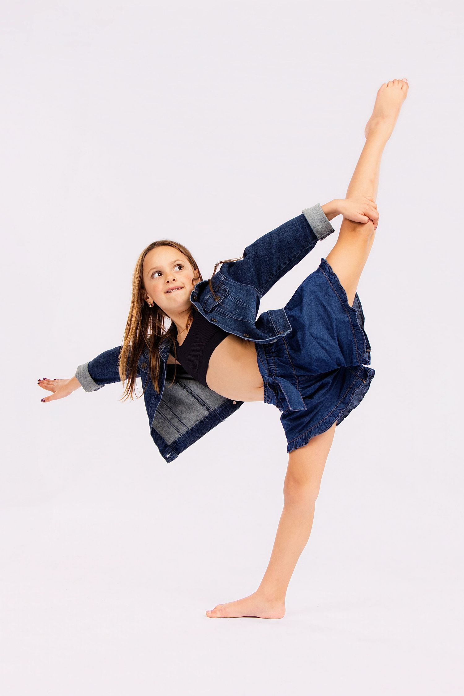 A dancer performs a high kick in a navy blue outfit against a white background.