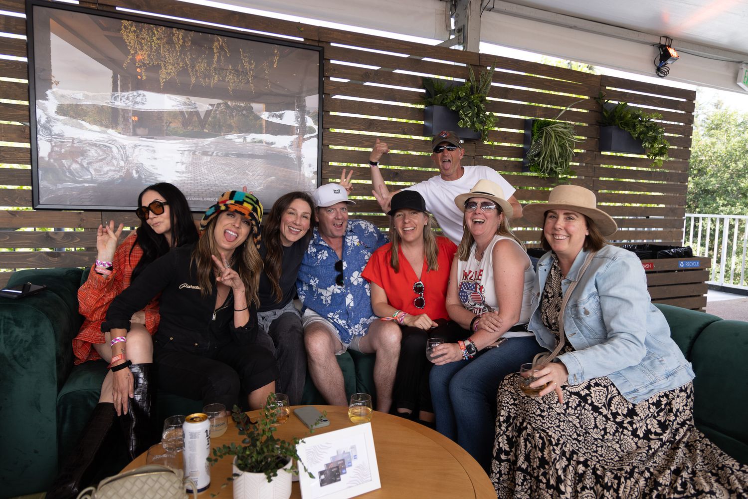 A group of seven women posing together at an outdoor event, smiling and wearing festive hats and colorful outfits.