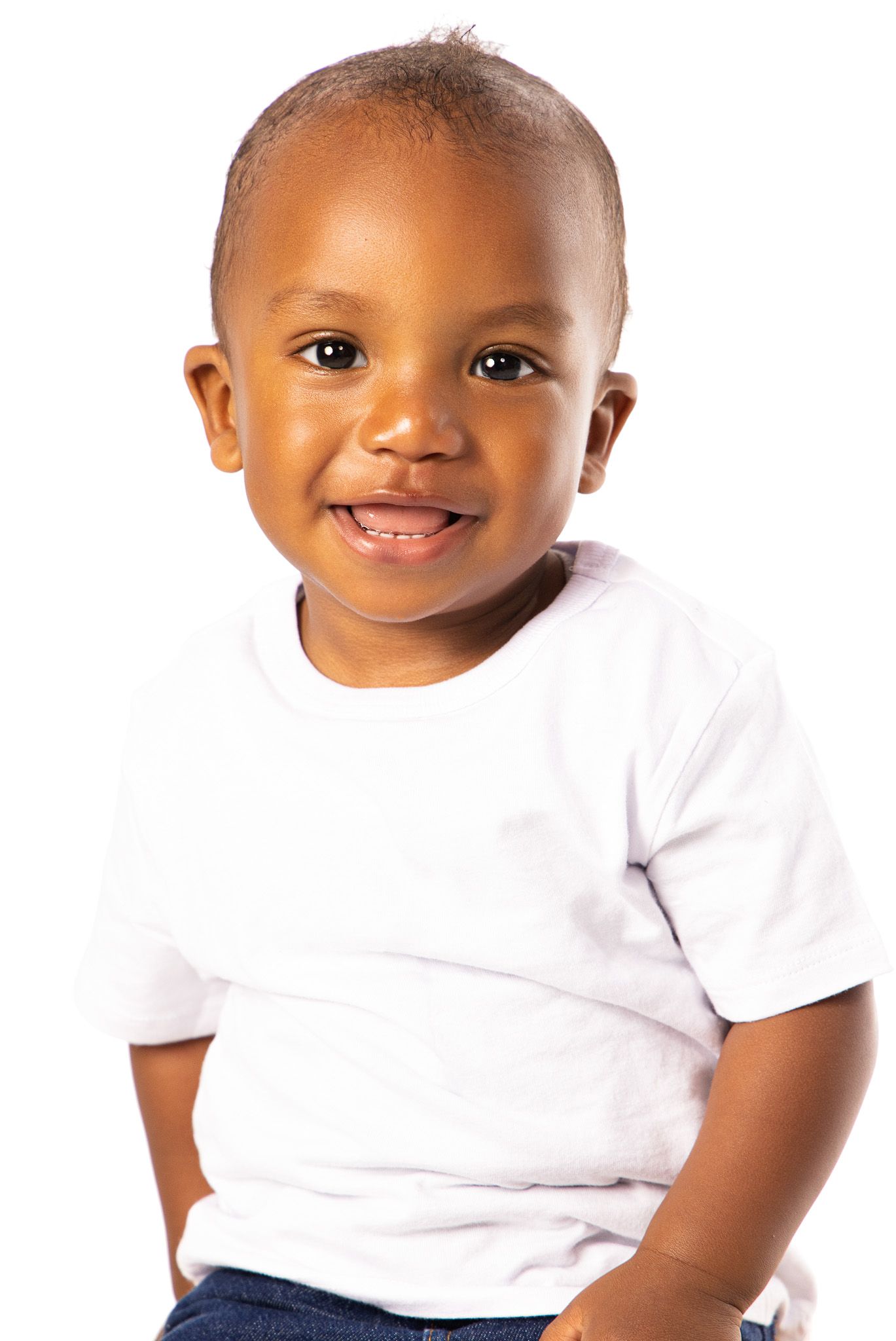 Baby wearing white t-shirt smiles brightly against white background in studio portrait.