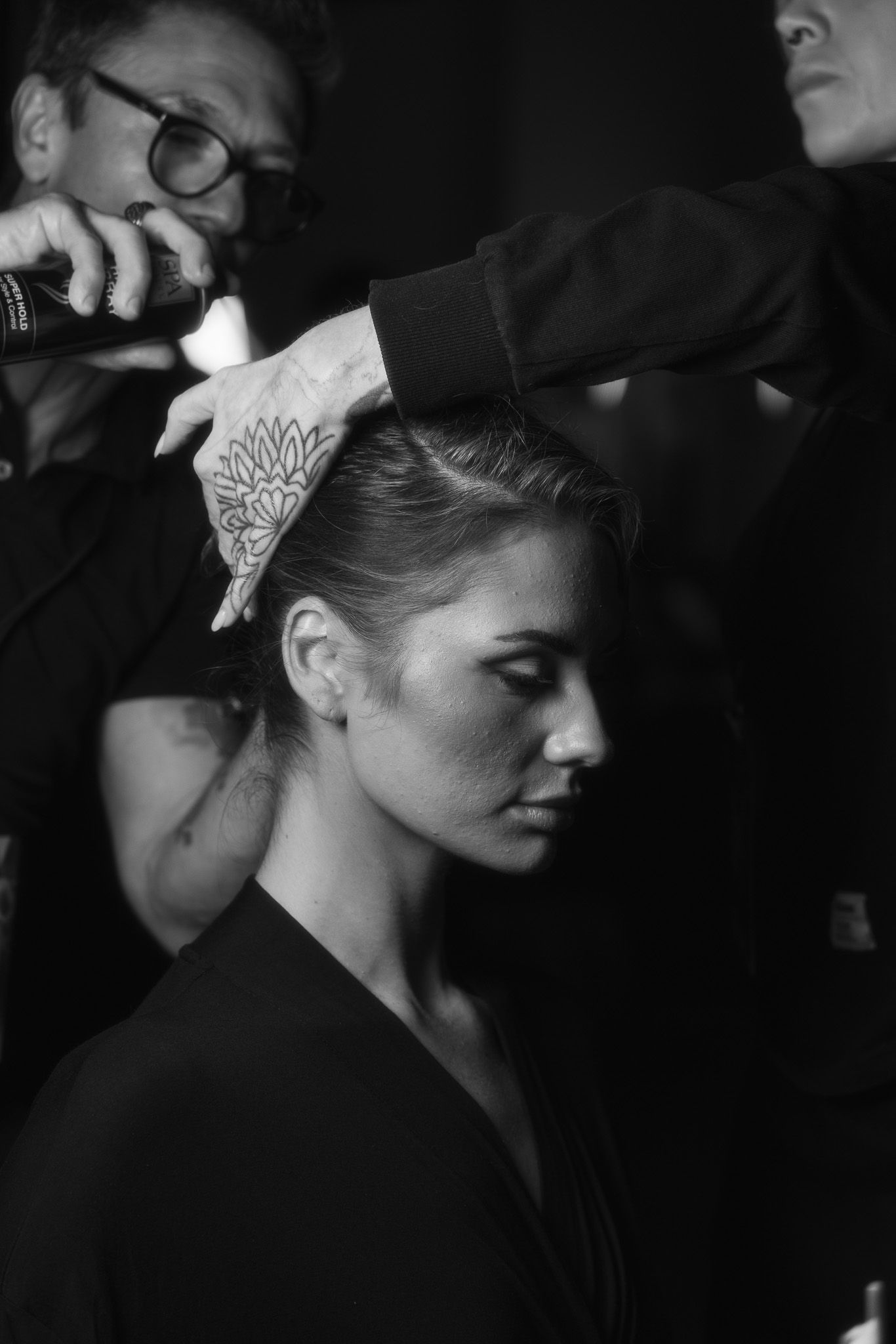 Black and white profile shot showing a delicate lotus flower tattoo behind the ear.