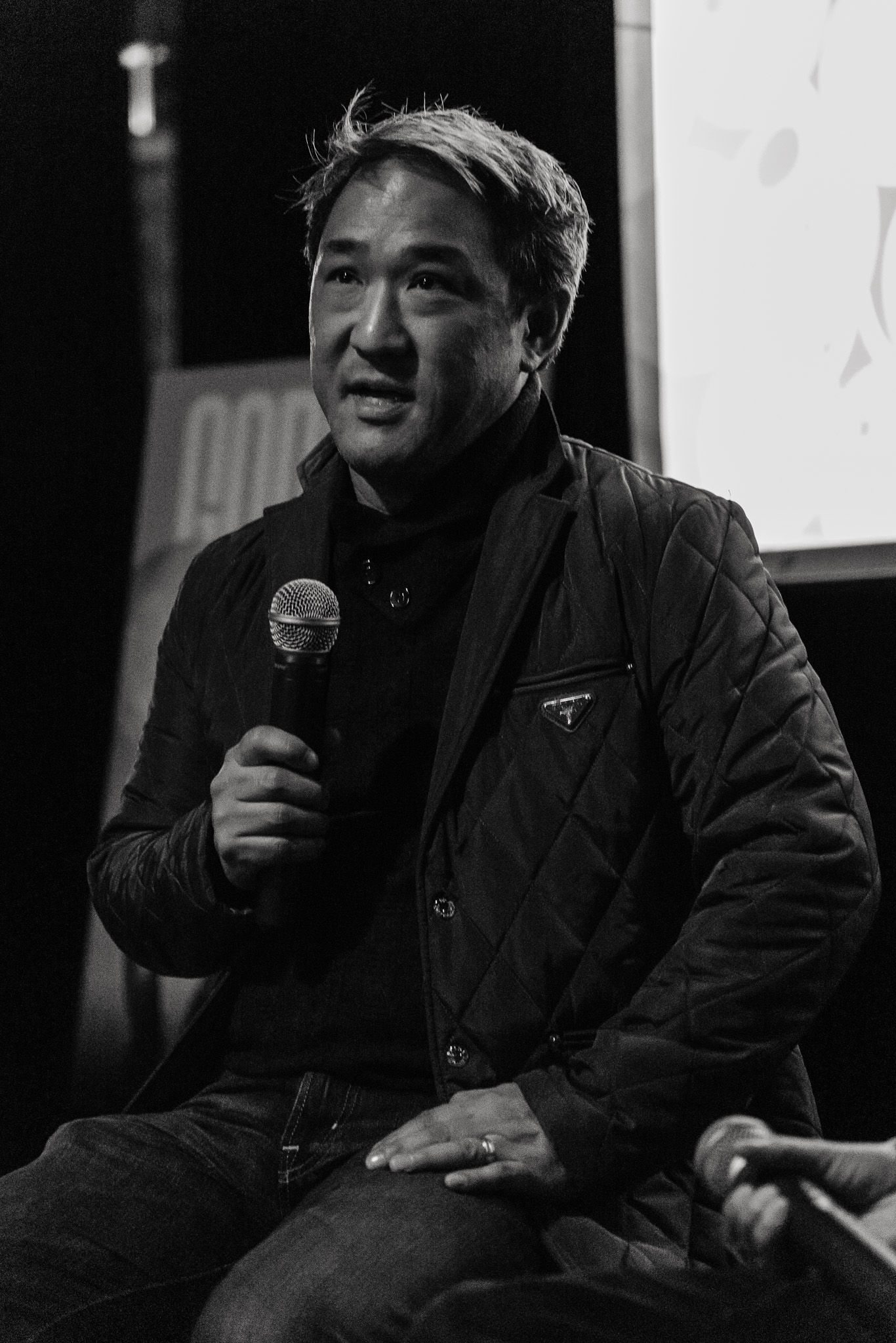 Black and white photo of a speaker holding a microphone during a presentation.