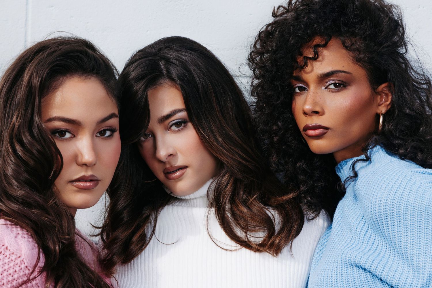 Fashion models wearing cozy sweaters pose together against a neutral background.