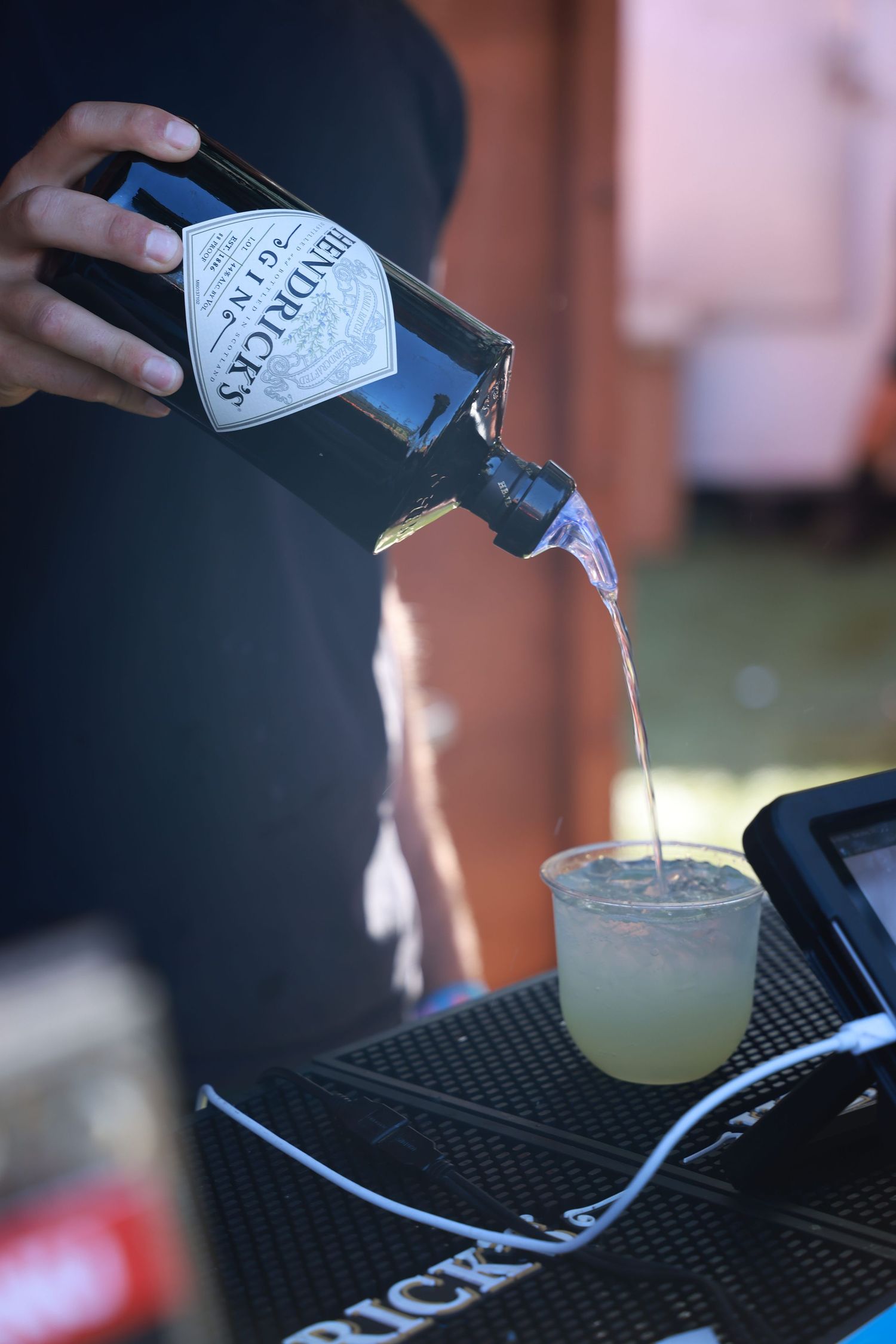 Pouring a craft cocktail from a Hendrick's gin bottle into a coupe glass on a black bar mat.