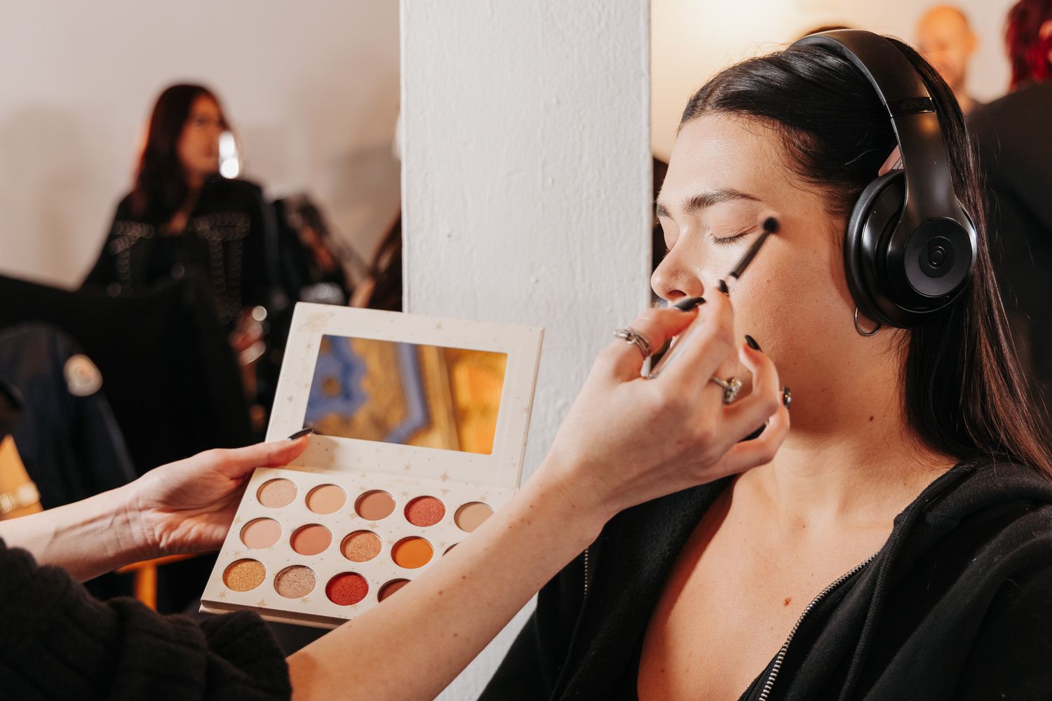 Professional makeup artist applies eyeshadow using a brush while holding a neutral-toned palette.