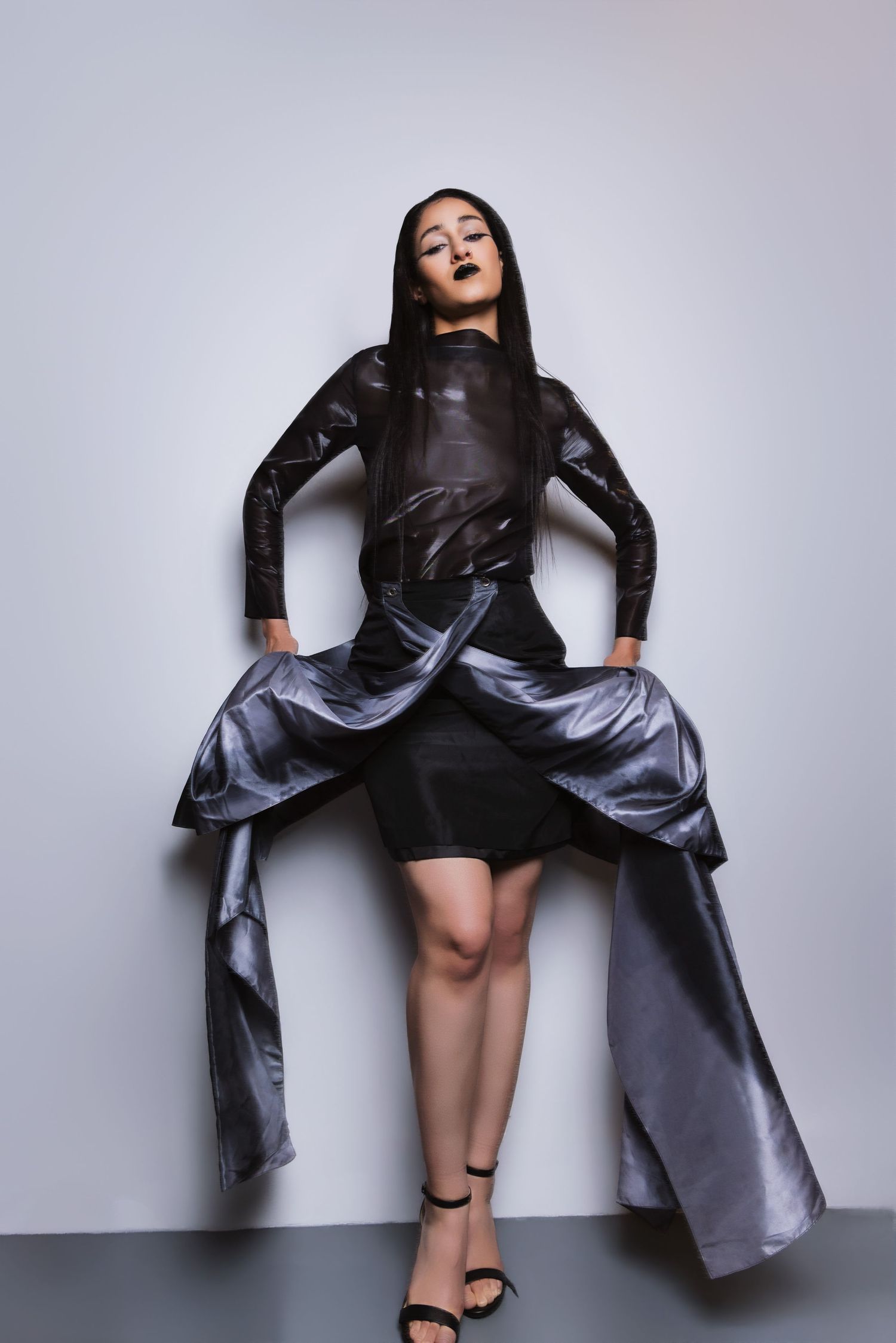 Fashion model in silver metallic coat and black dress poses dynamically against white background in editorial series.