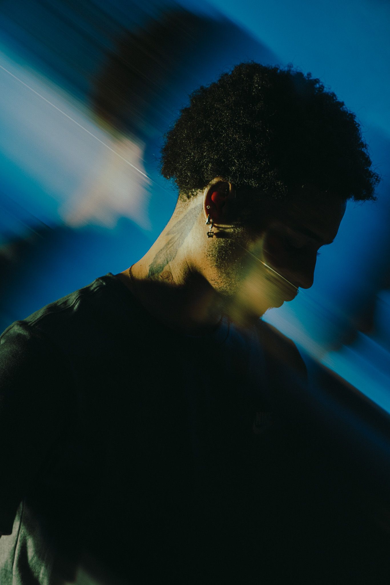 Young Black man with curly hair and neck tattoo photographed in dramatic blue studio lighting.