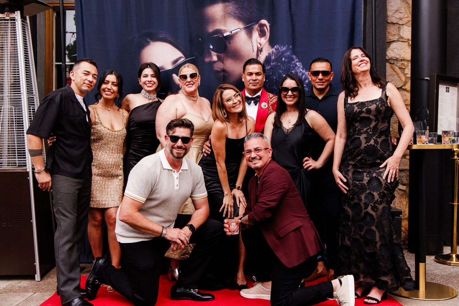 A diverse group of elegantly dressed people posing together on a red carpet at a glamorous event.