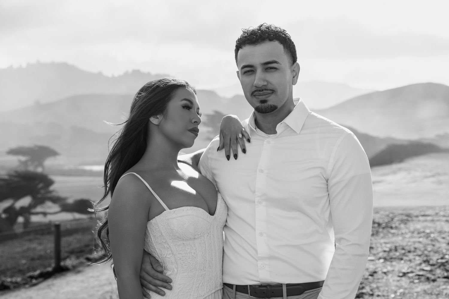 A romantic couple embraces against a scenic mountain backdrop during a black and white photo session.