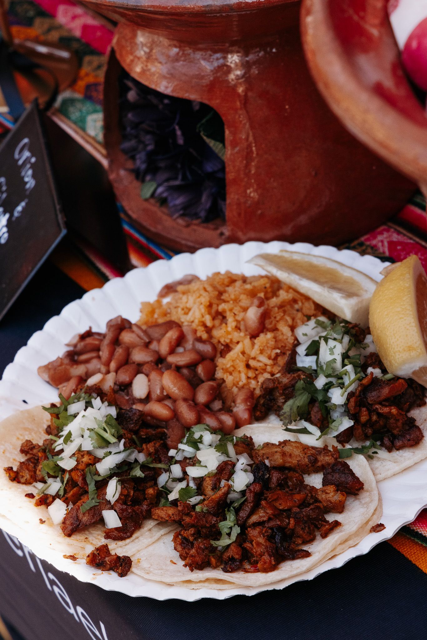 Sequence of street tacos being assembled with meat, beans, onions and cilantro on corn tortillas.