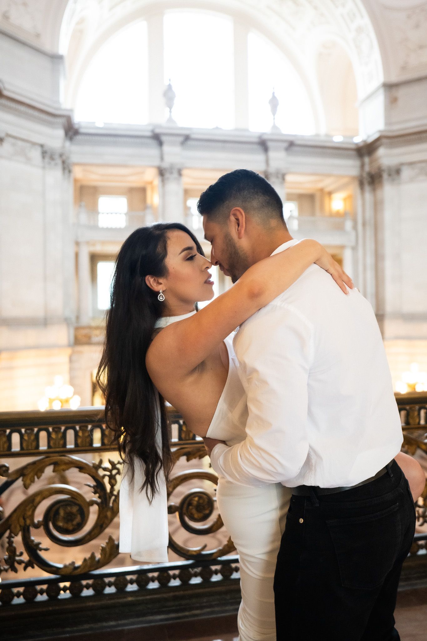 A romantic couple shares an intimate dance and kiss in an elegant venue with ornate architectural details.