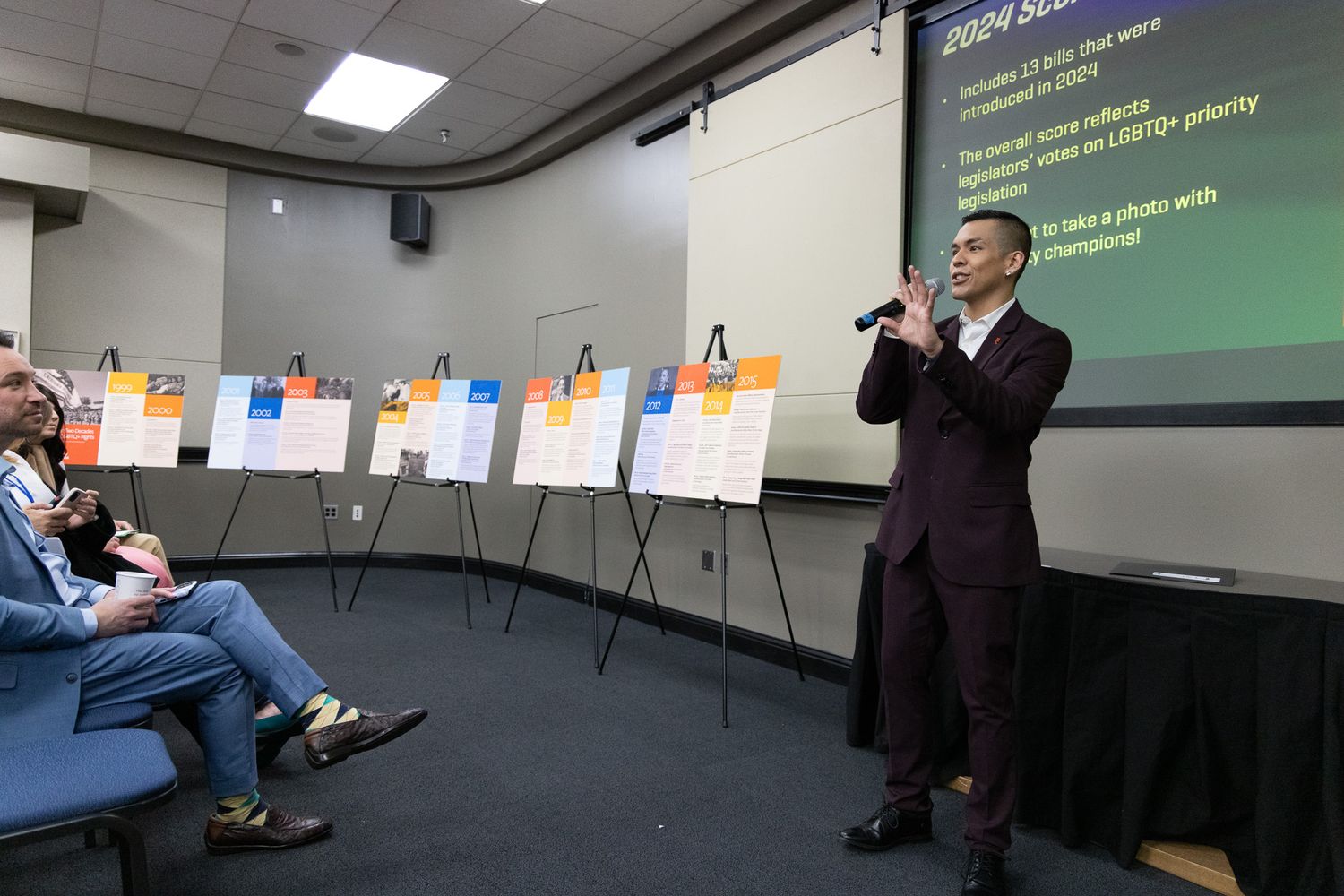 Business professionals gather in a modern conference room with presentation slides displayed on multiple screens.