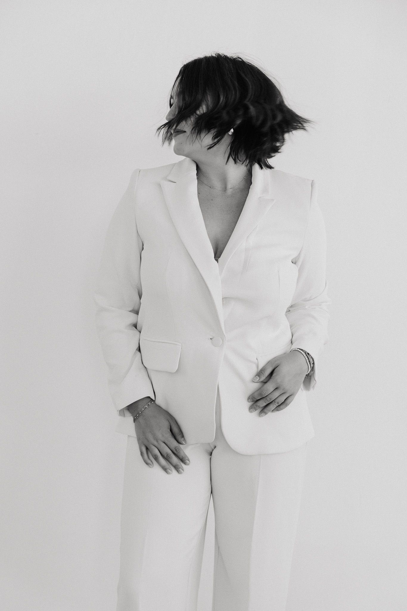 Black and white artistic portrait series showing figure dressed in crisp white suit, shot against minimalist backdrop.