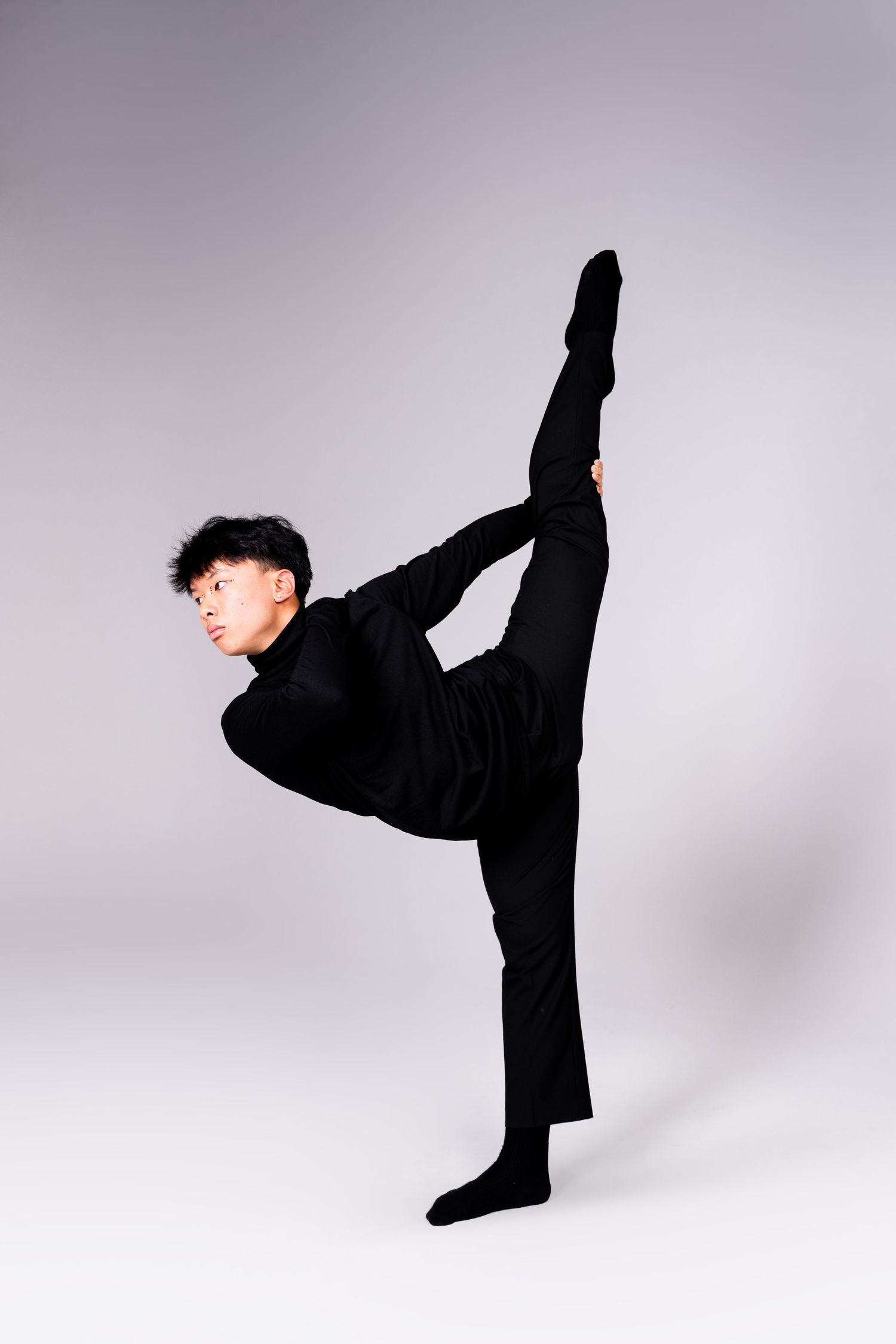 Athletic performer in black demonstrates martial arts kicks with precise form against neutral background.