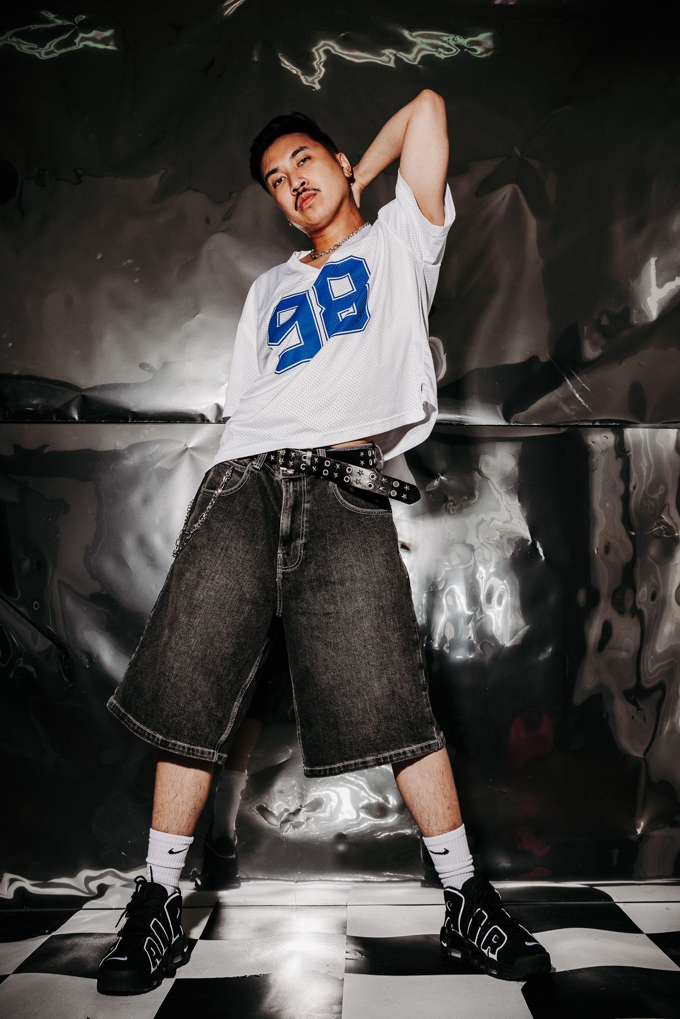 Dynamic urban fashion photo on checkered floor with white jersey number 38, baggy jeans and stylish sneakers.
