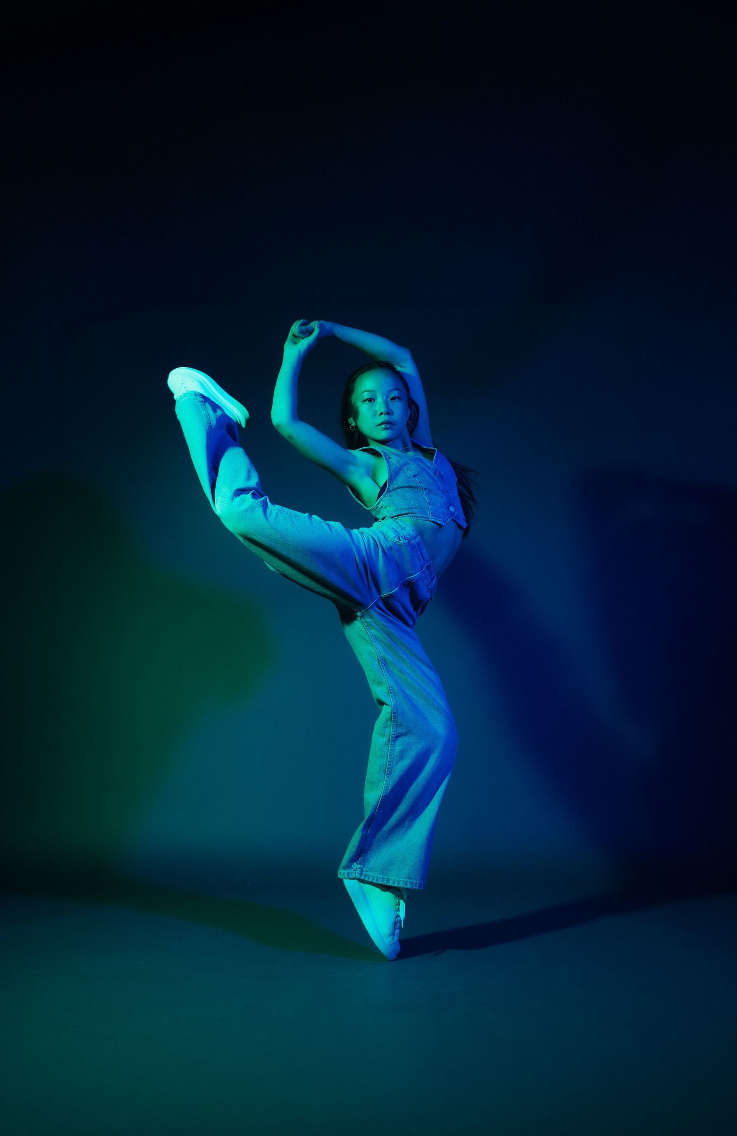 Modern dance performance captured in cool blue-green lighting showing expressive arm movements.