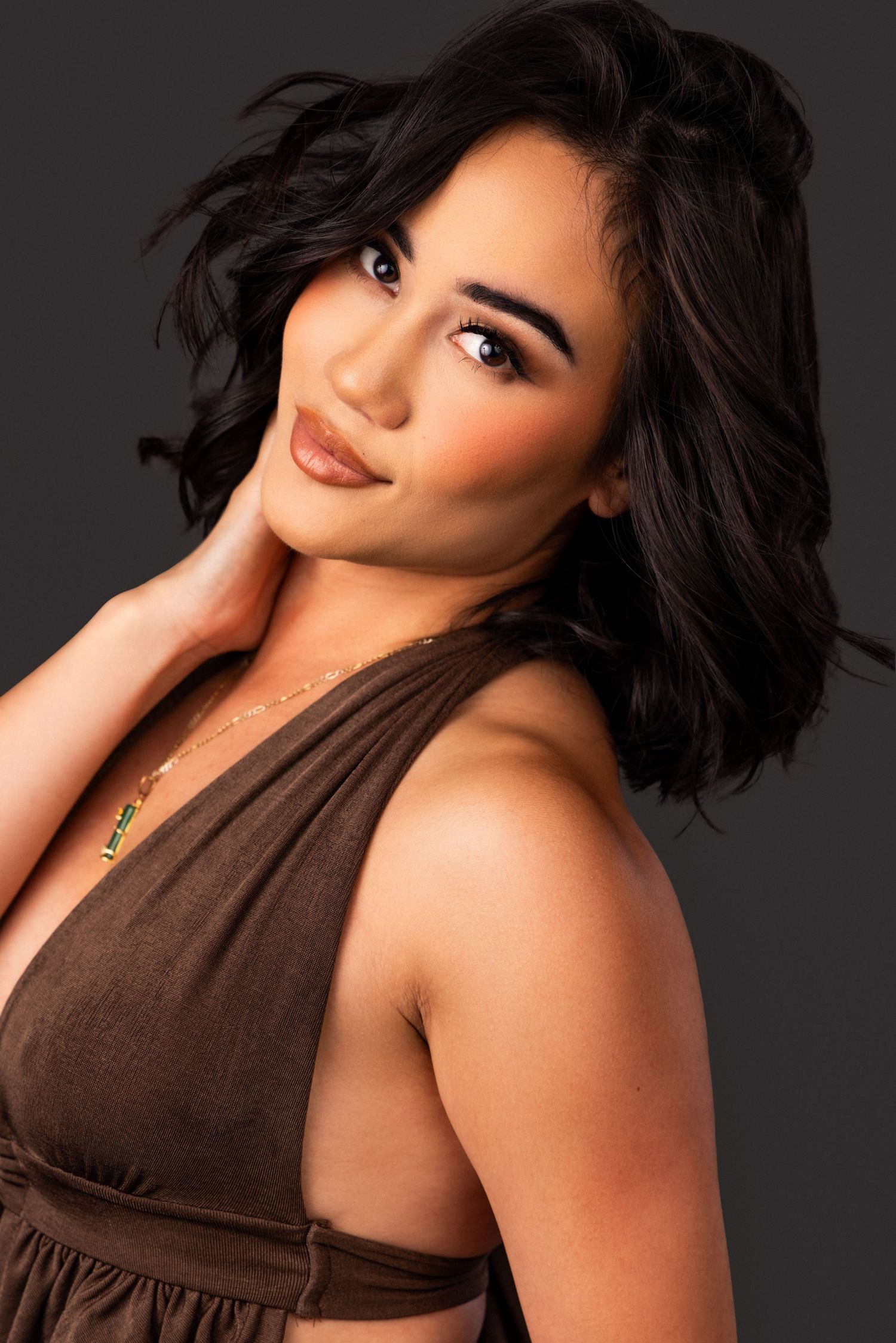 Studio portrait of a person in a brown halter top against a dark background.