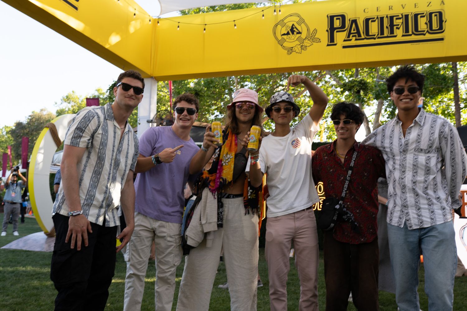 Group of friends posing under a Pacifico beer branded yellow arch at an outdoor festival event.