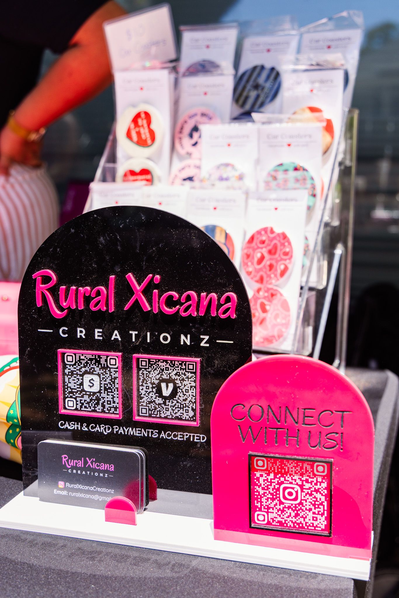 Rural Xicana Creationz vendor display with QR codes, business cards, and colorful products.