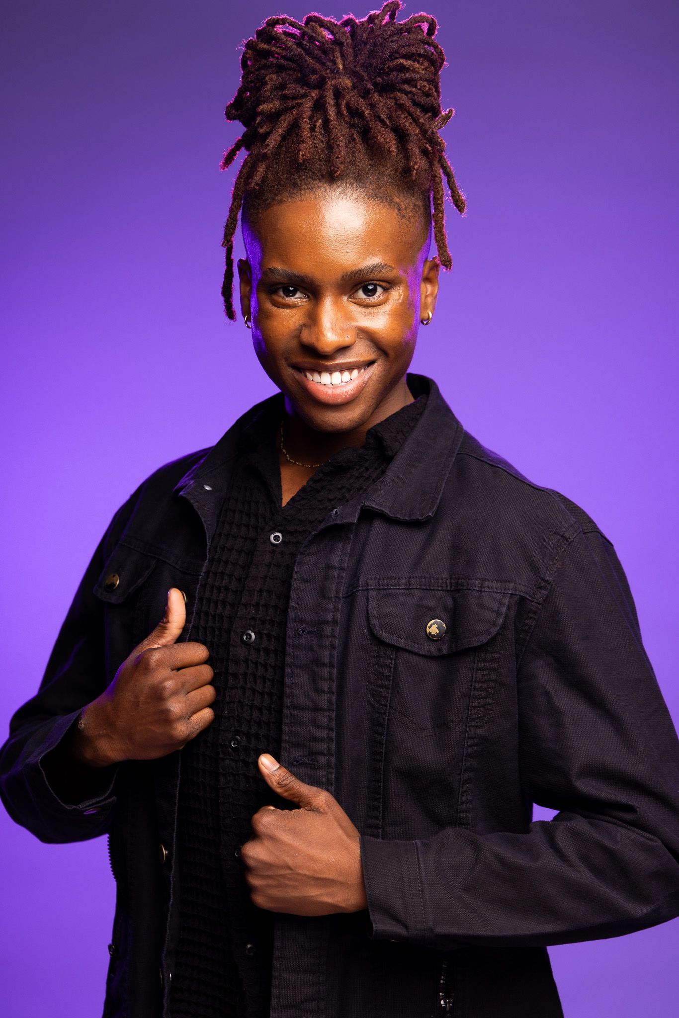 Cheerful portrait with burgundy locs hairstyle giving thumbs up against purple background.