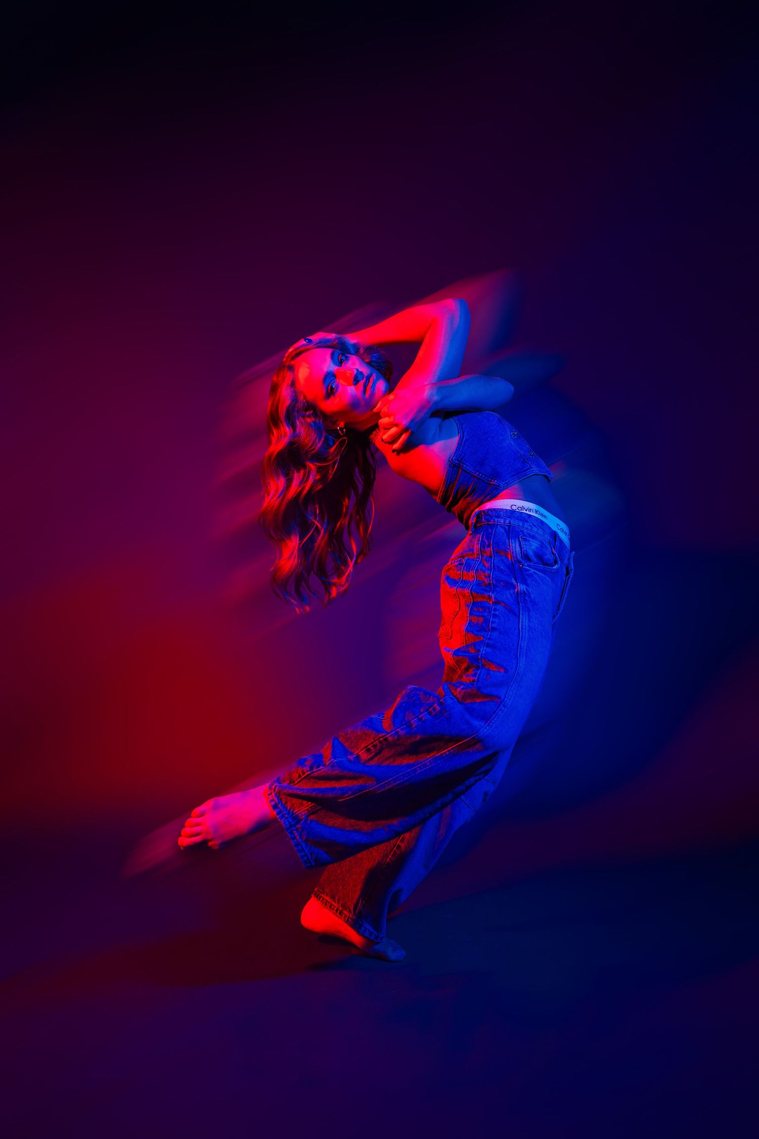 Dynamic dancer leaping through space under vibrant red and blue lighting effects.
