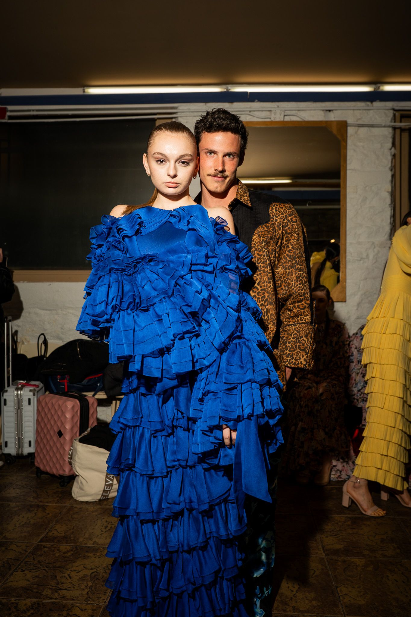 A dramatic fashion sequence showing a model in a ruffled bright blue gown posing against a dark background.