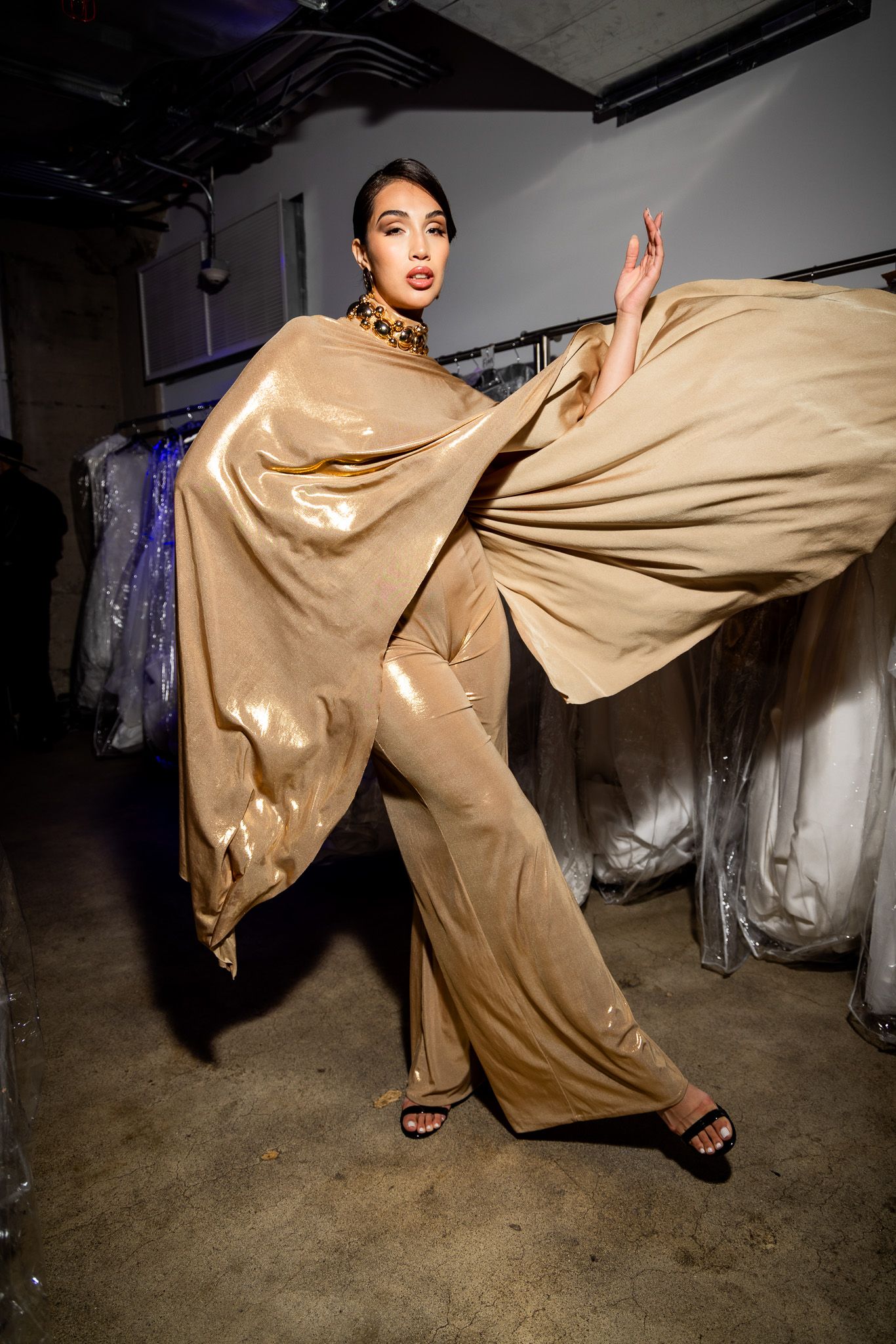 A dynamic fashion sequence shows a model in flowing gold fabric making dramatic kicking movements against a dark background.