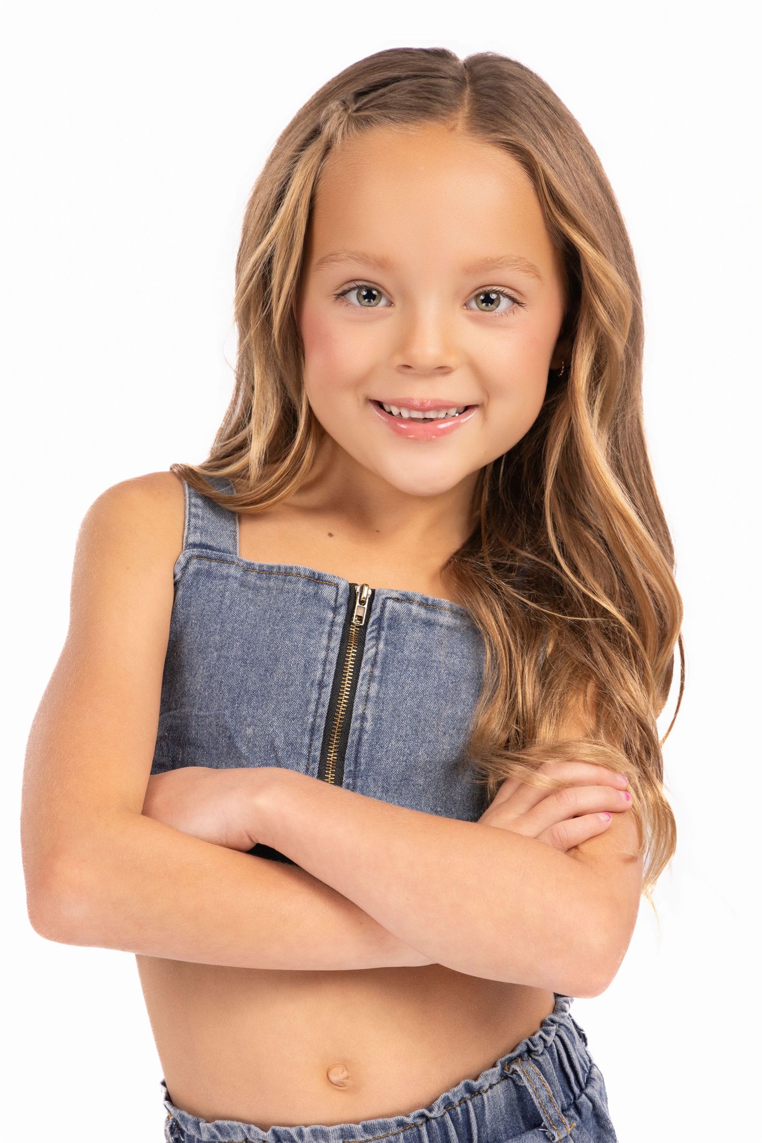 Child model in denim crop top poses confidently with crossed arms.